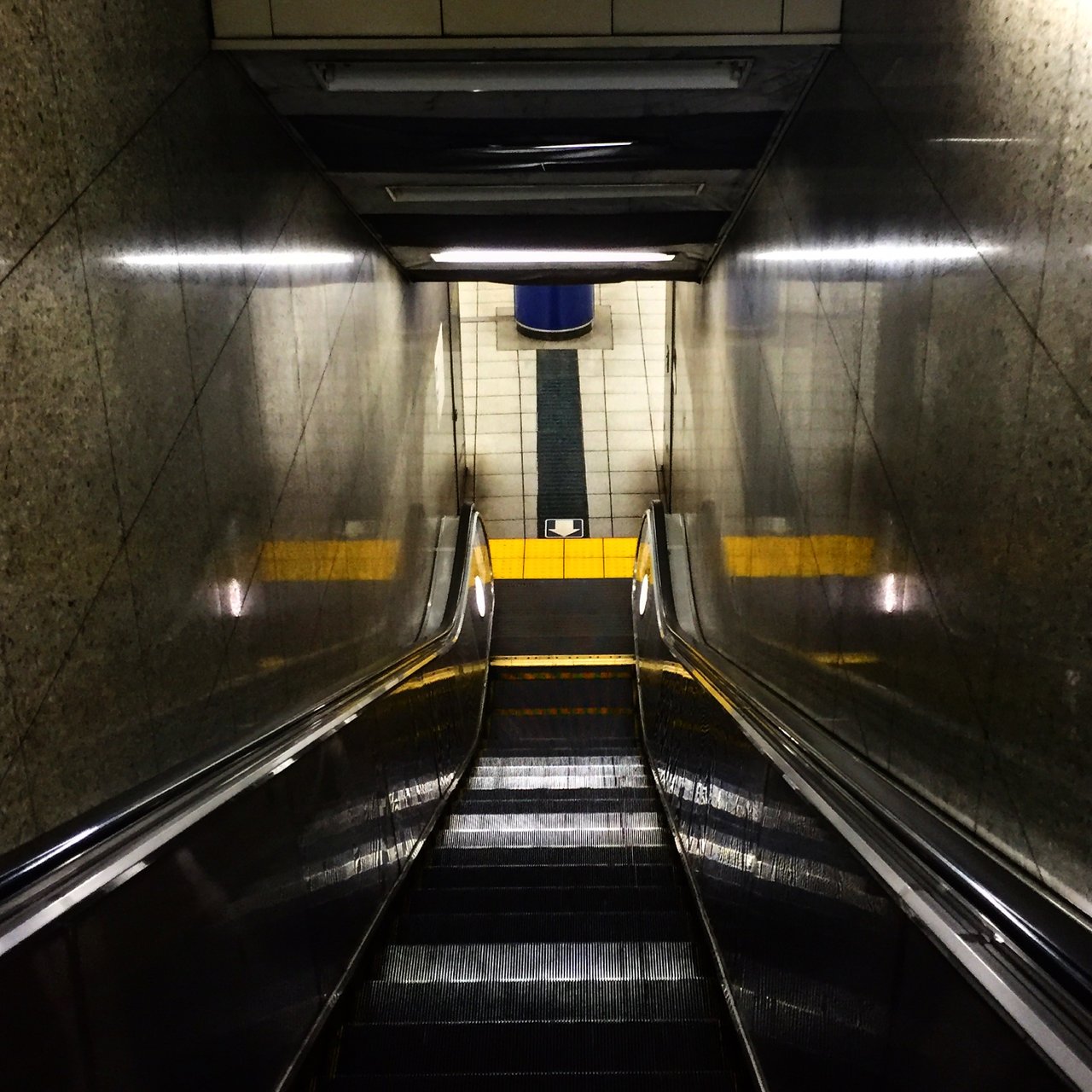 Empty escalator descending into a subway station, monochrome tones