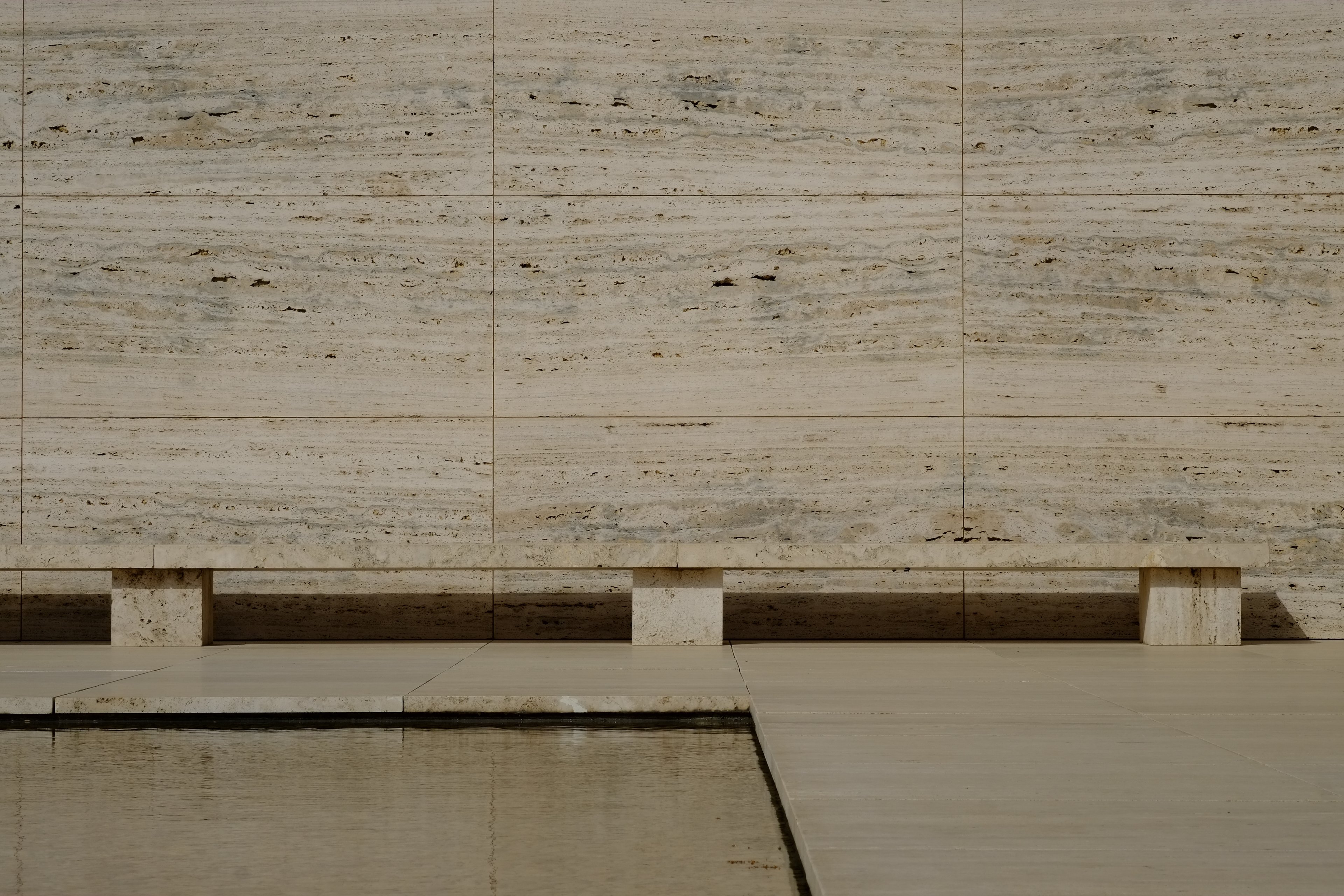Travertine wall and bench beside a still reflecting pool