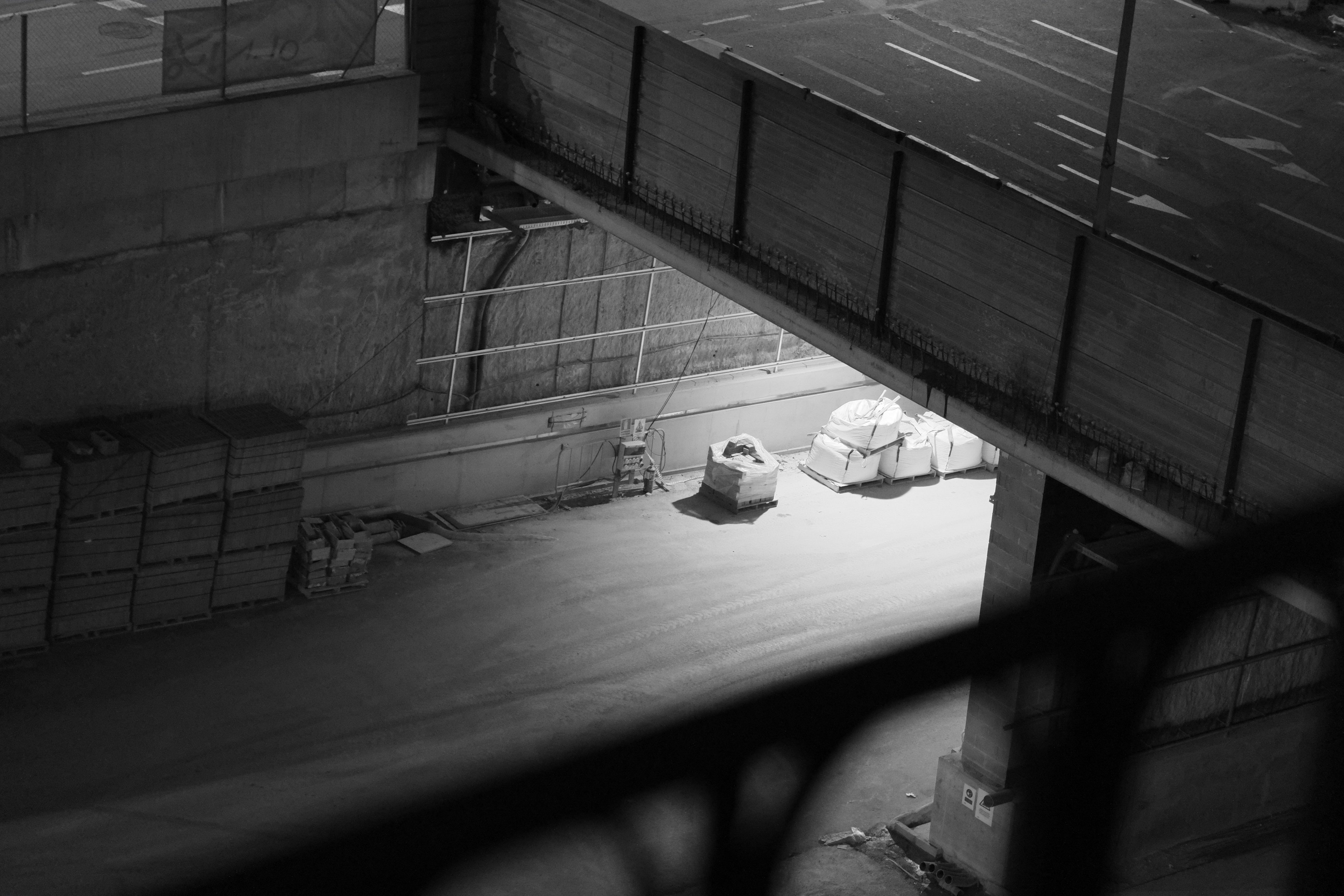 Construction yard beneath a road bridge at night, pallets and sacks in a pool of light
