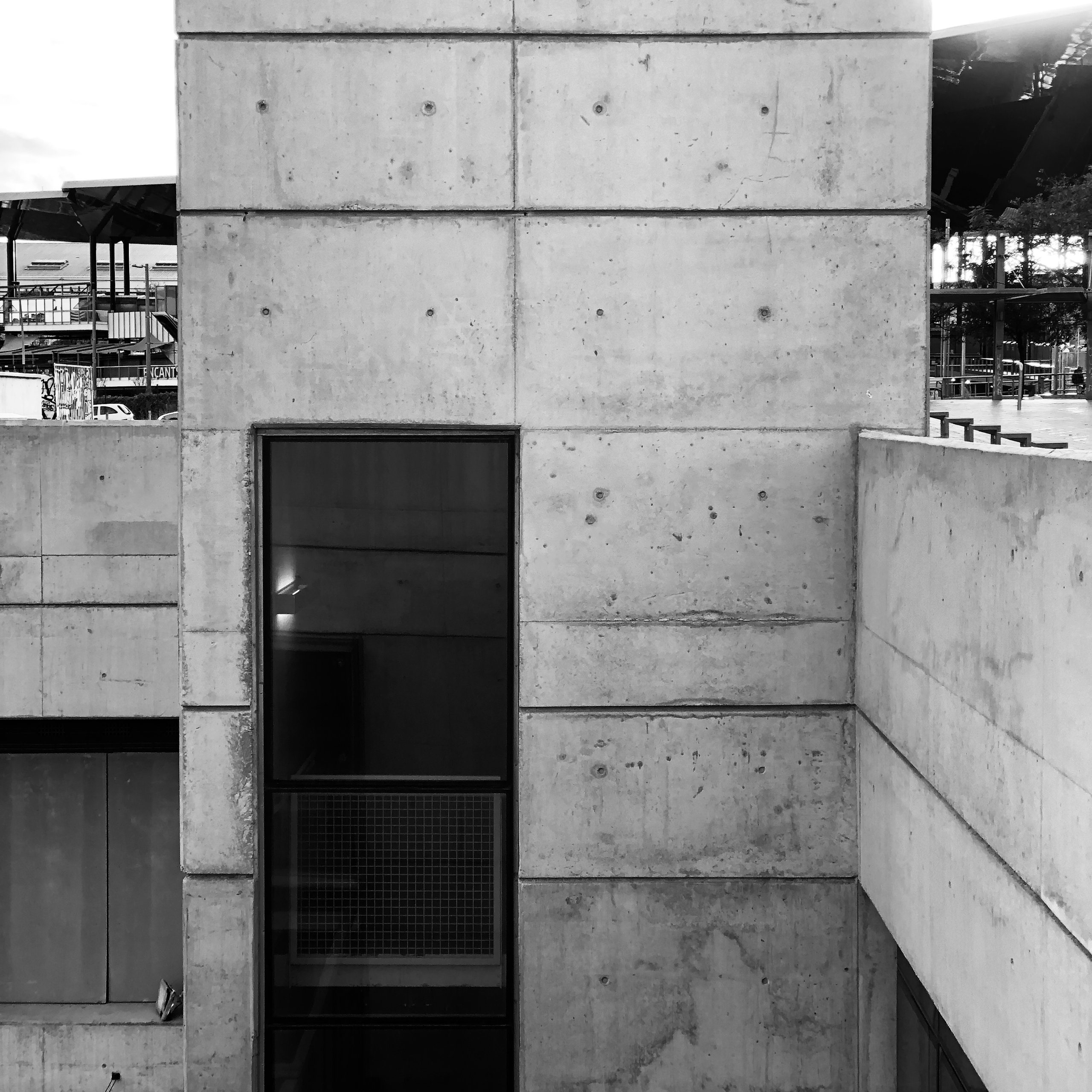 A raw concrete tower with a slot window, market canopies beyond