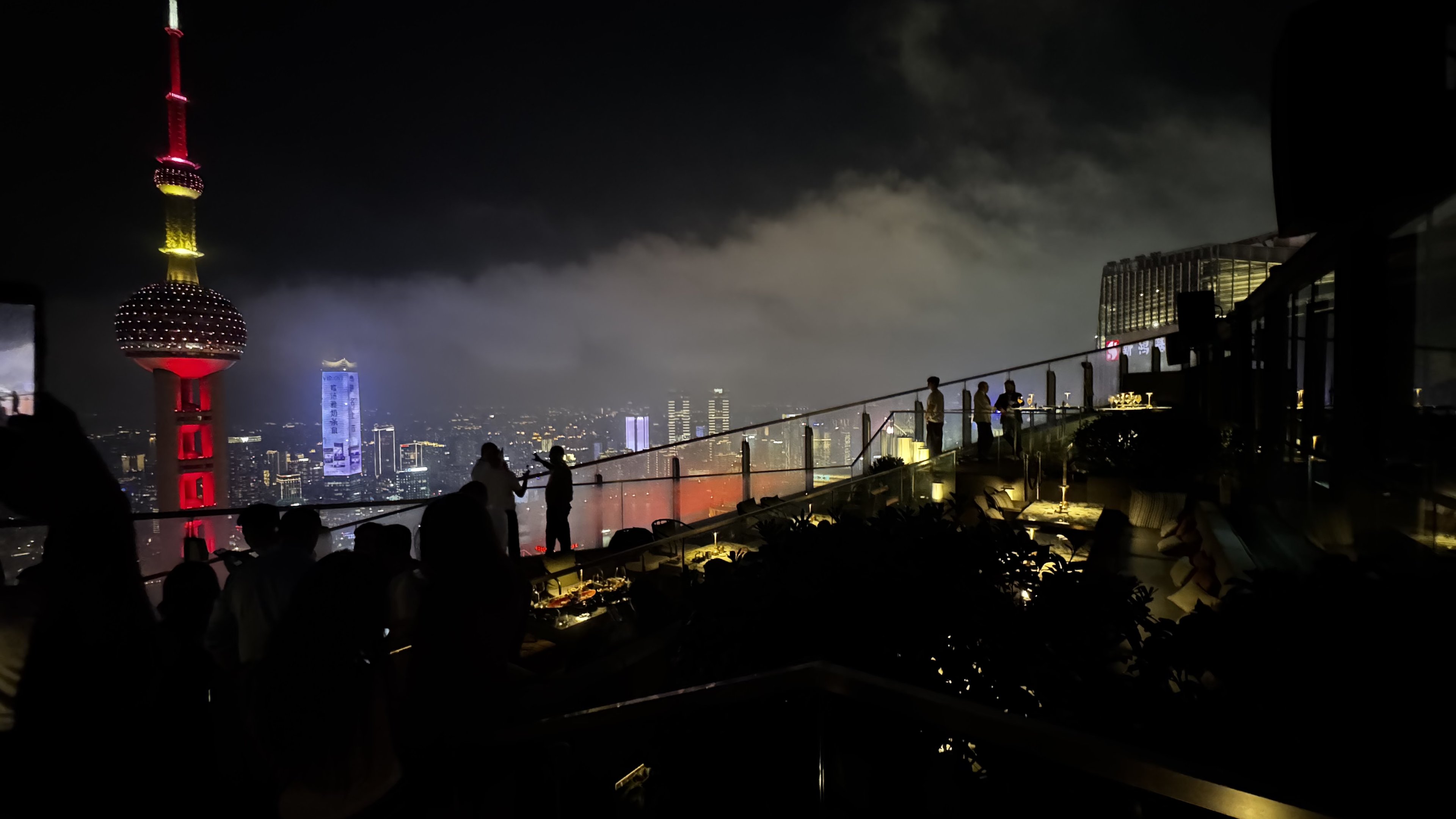 The Oriental Pearl Tower lit red above low cloud, from a rooftop terrace