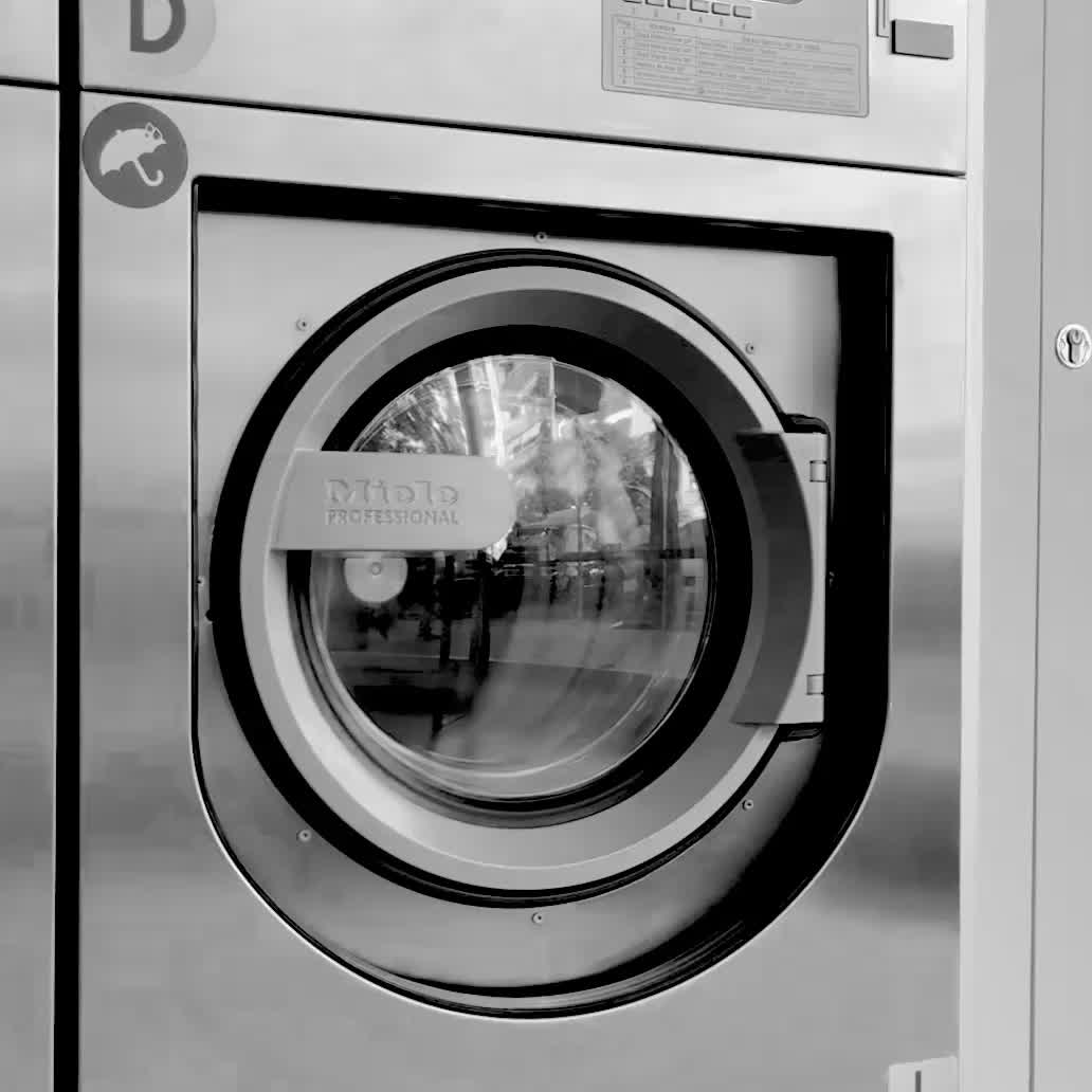 A laundrette drum tumbles behind its porthole, the street reflected in the glass