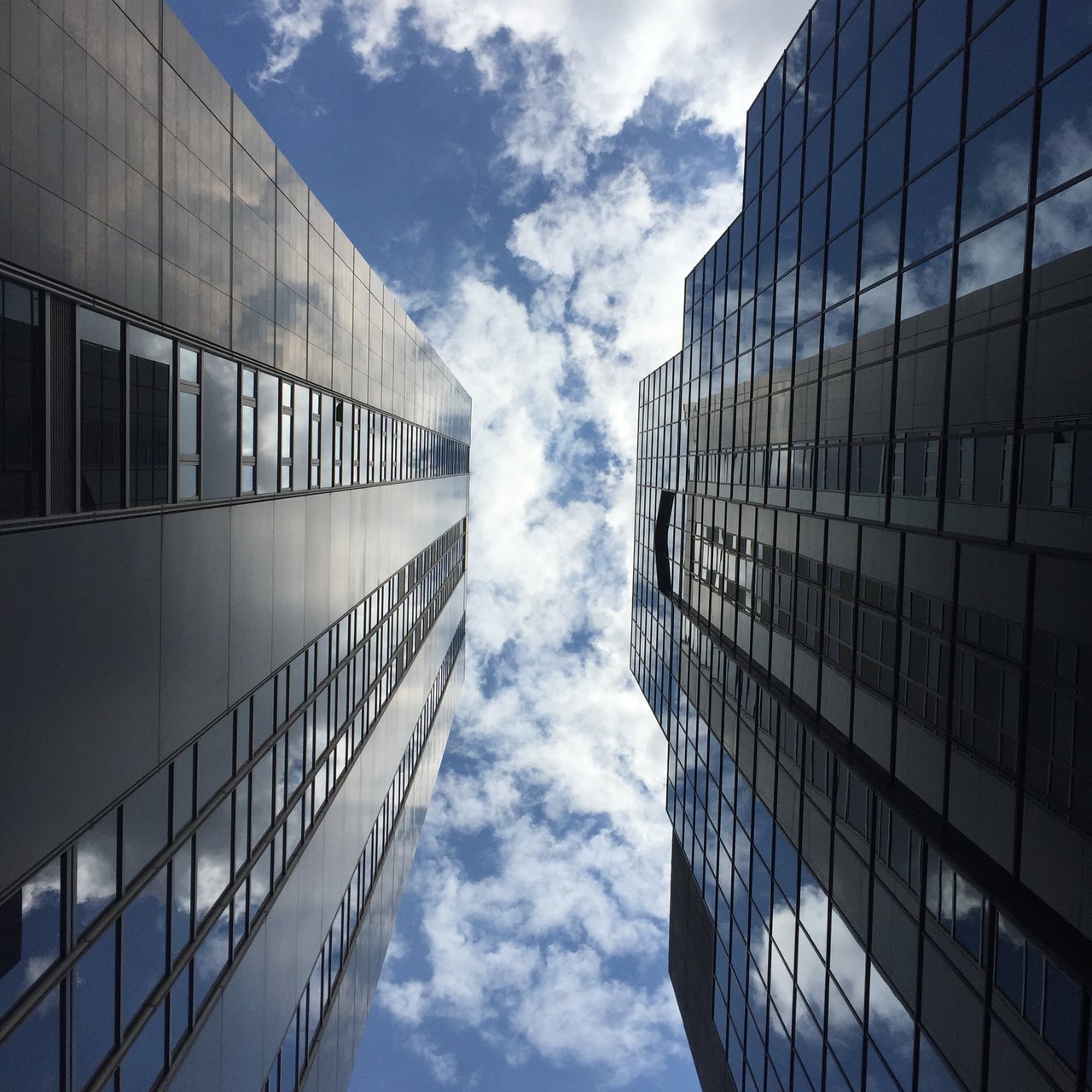Two glass office façades converging on a strip of clouded sky