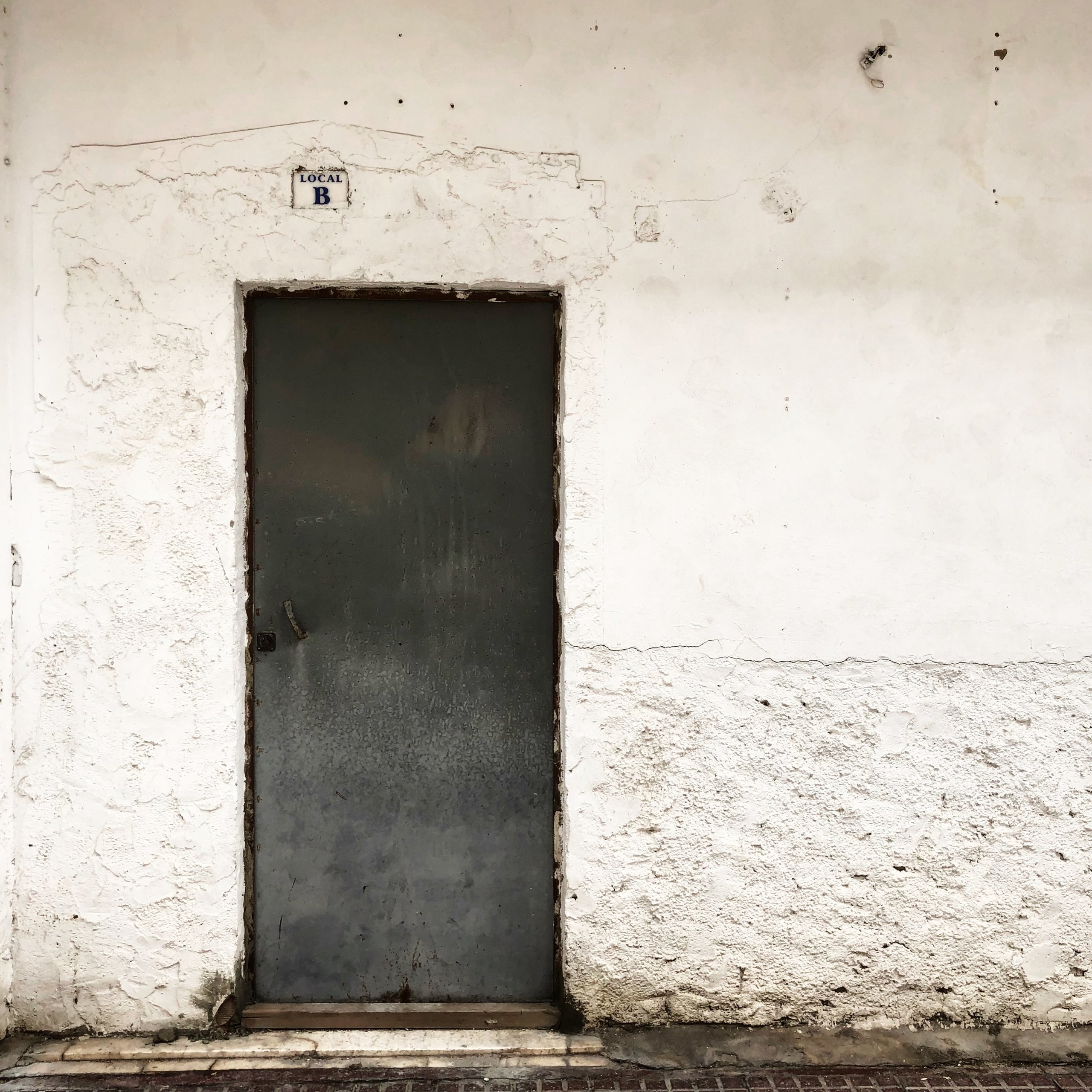 A grey steel door in a weathered whitewashed wall, tiled LOCAL B above