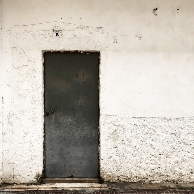 A grey steel door in a weathered whitewashed wall, tiled LOCAL B above