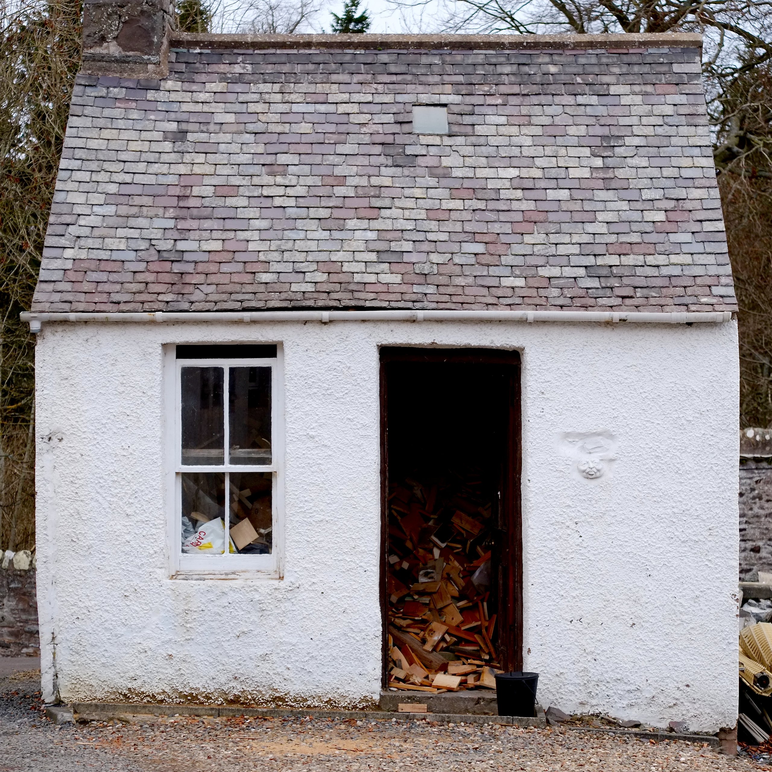 Whitewashed stone hut with slate roof, firewood stacked in the doorway