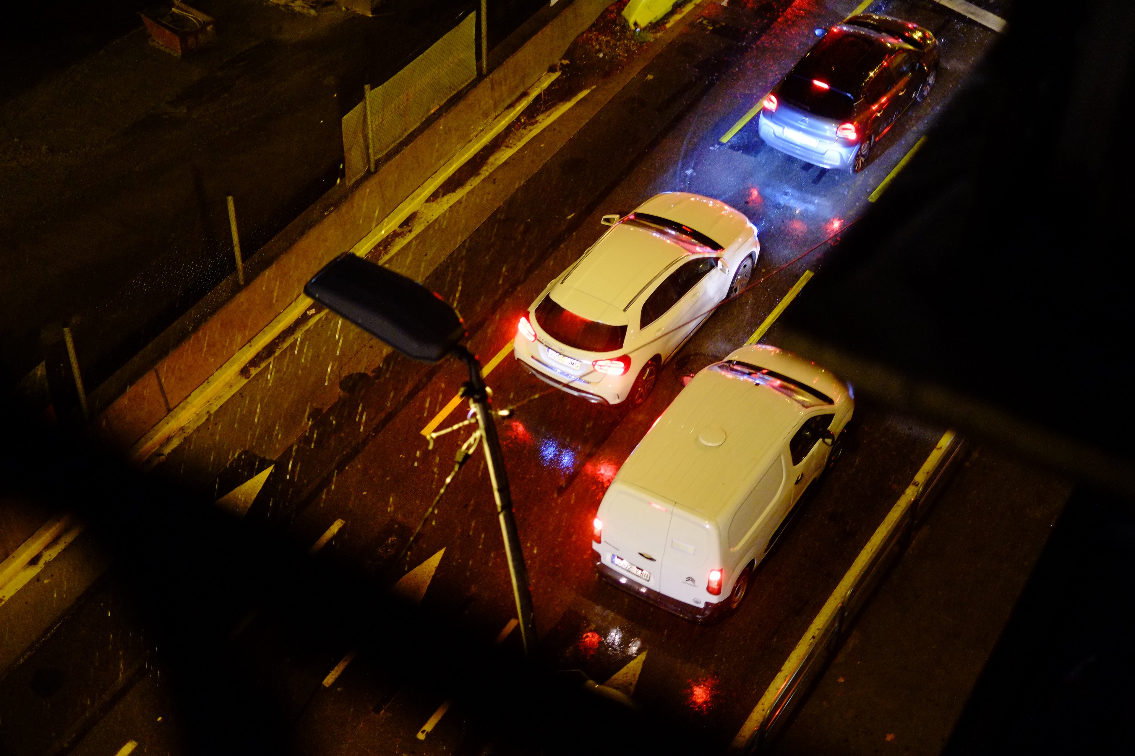 Cars queue on a rain-soaked street at night, seen from above