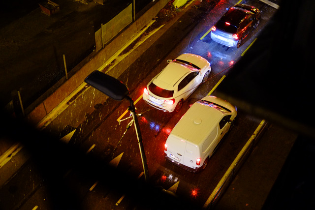 Cars queue on a rain-soaked street at night, seen from above