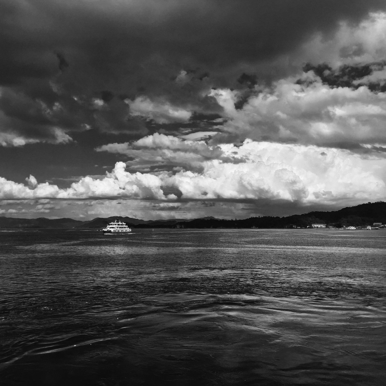 Wide monochrome seascape, towering clouds over a distant ferry