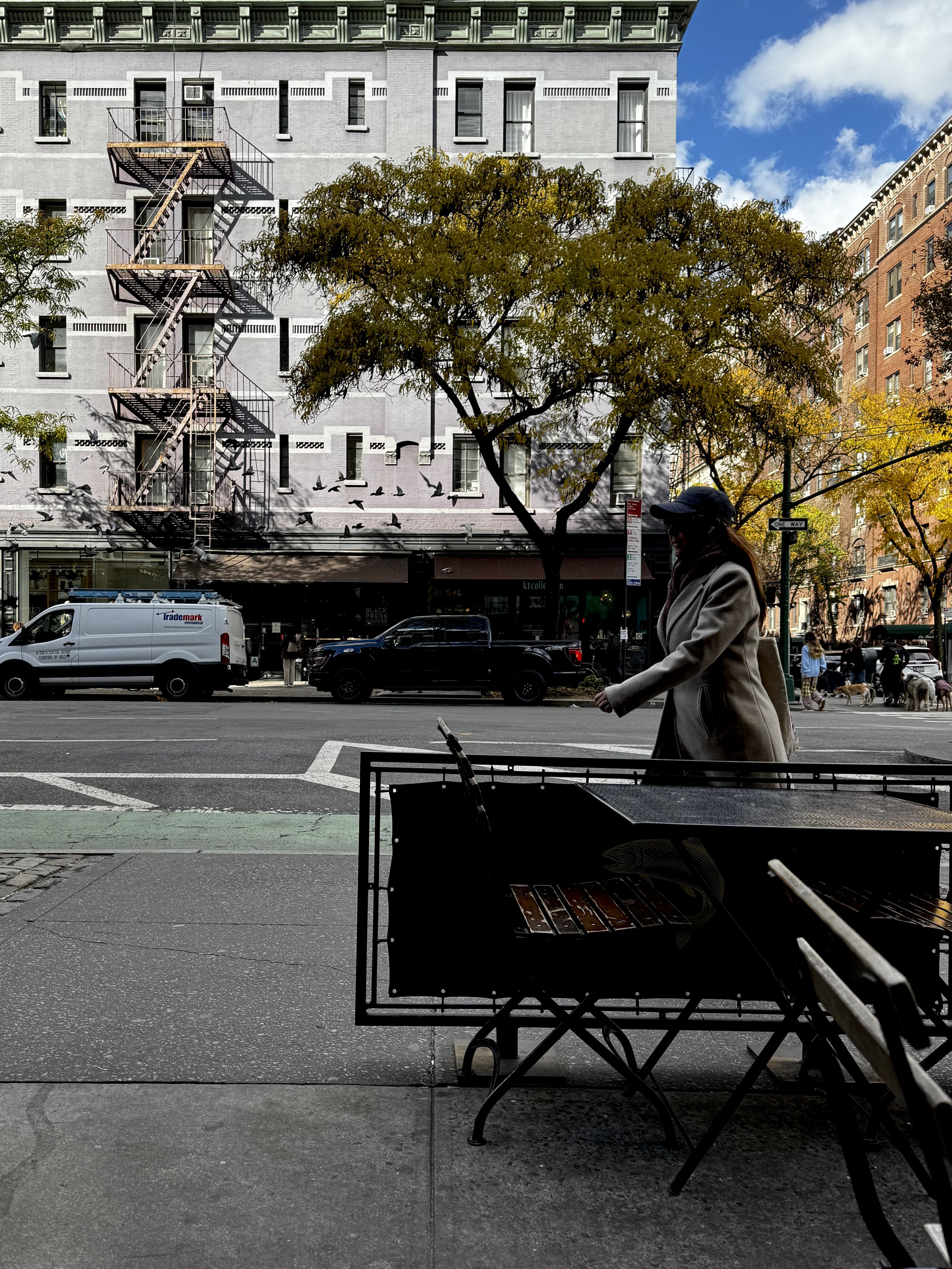 Pigeons burst past a lavender corner building as a woman crosses the street