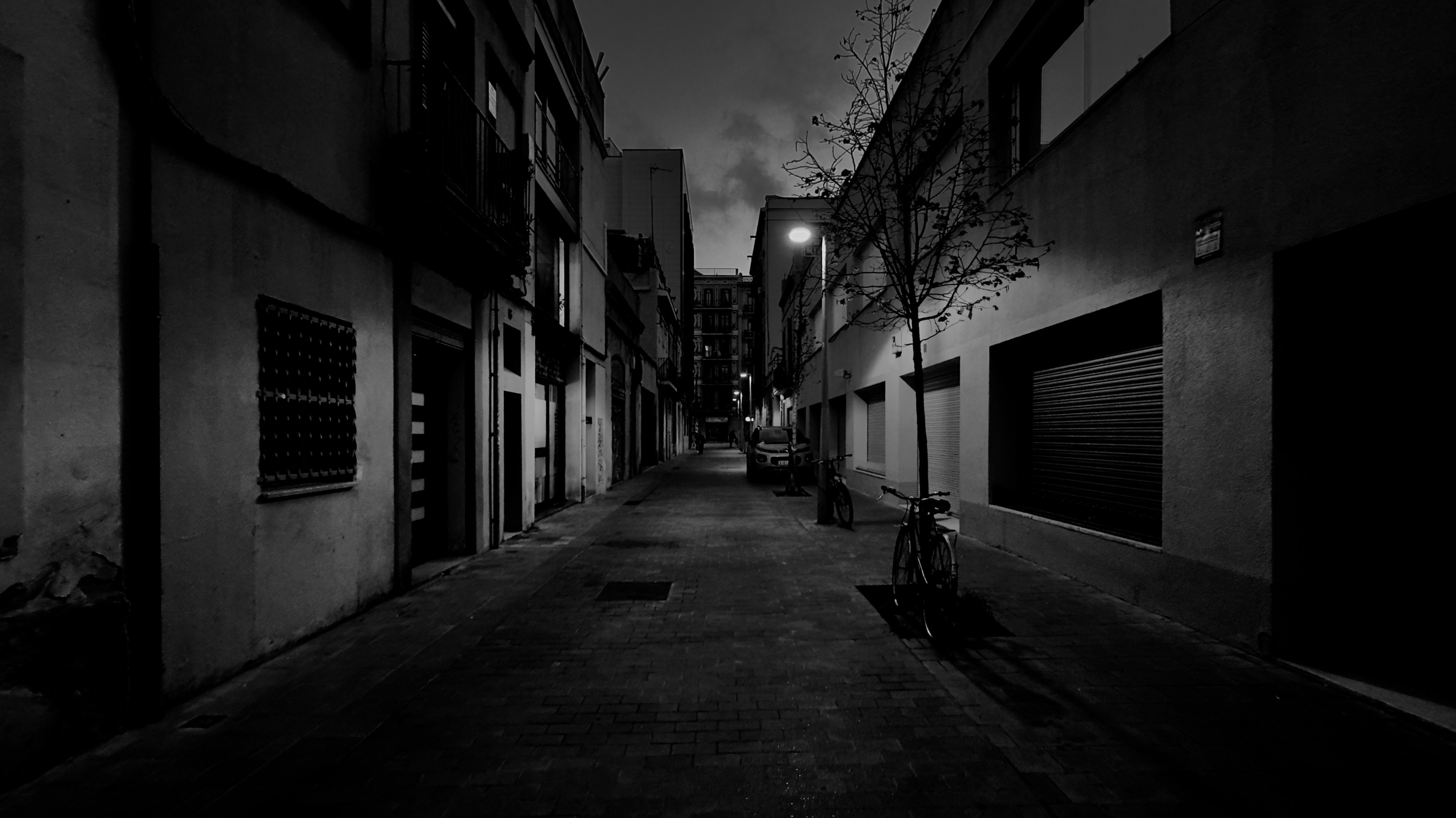 An empty lane at night under a single streetlamp, bicycles at the kerb