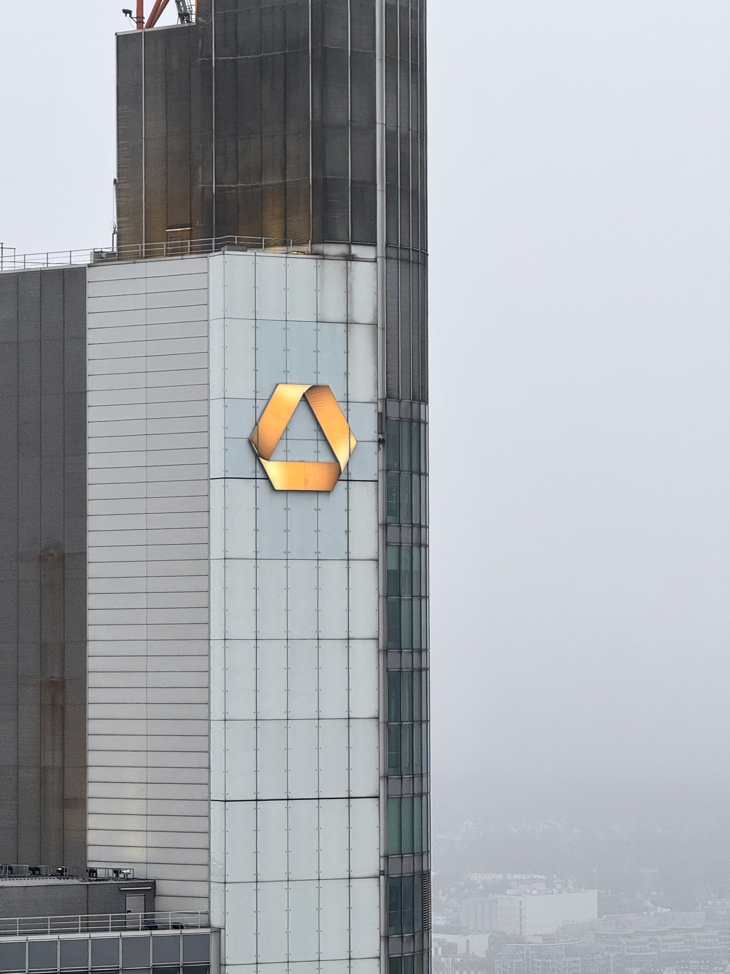 The Commerzbank logo glows on a tower shoulder as fog swallows the city