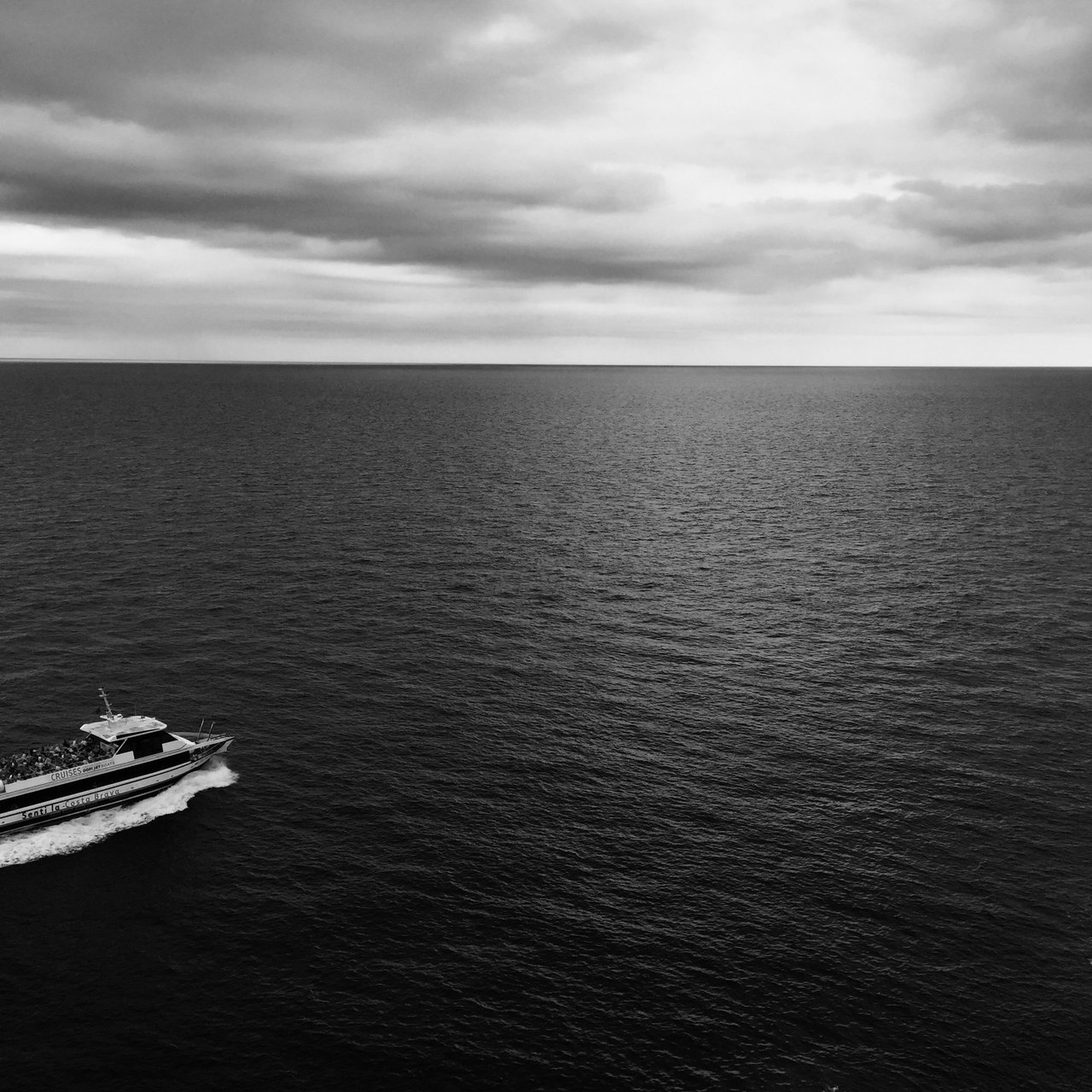 Small boat crossing a wide calm sea beneath a low cloud band