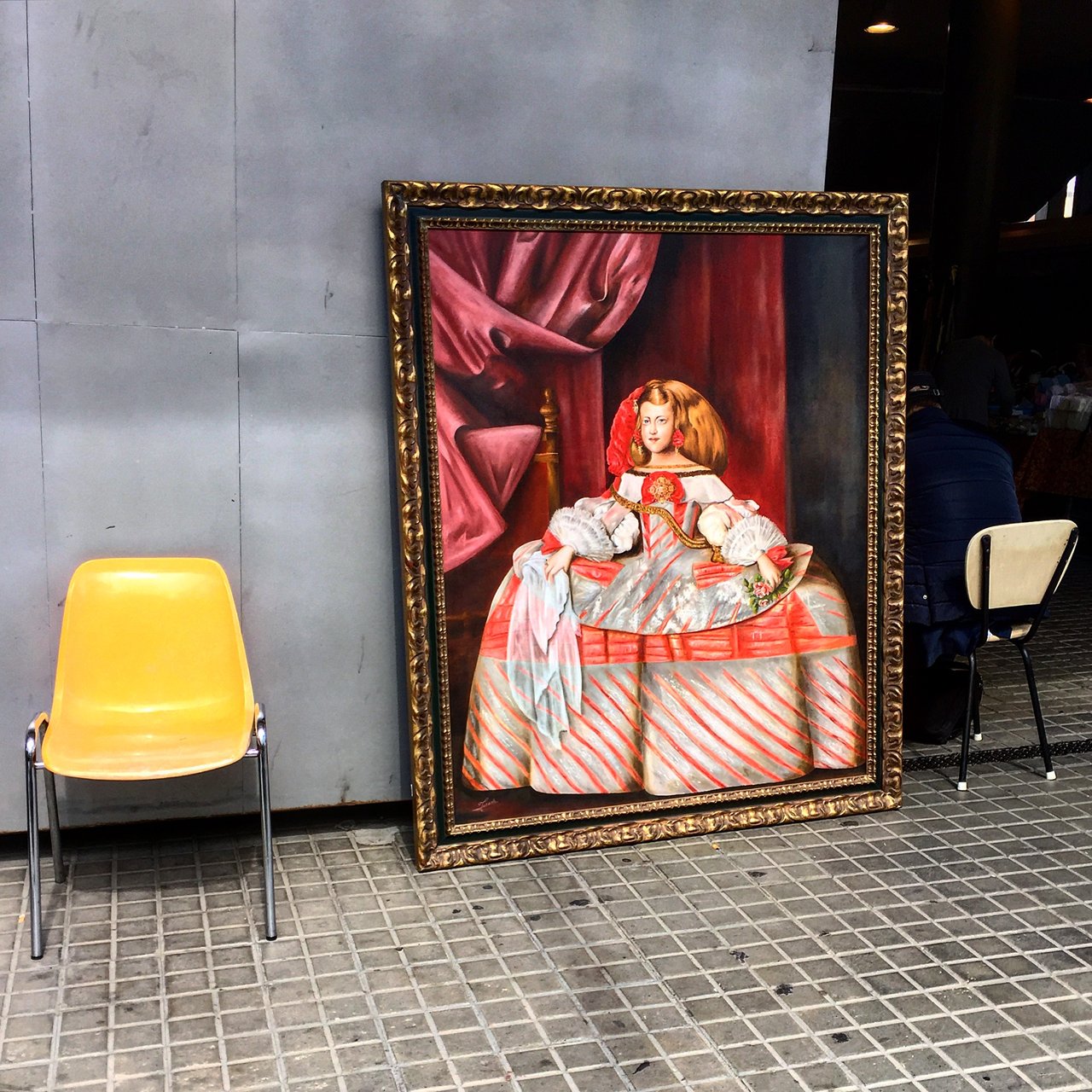 Framed reproduction of Velázquez's Las Meninas propped against a wall beside a yellow chair