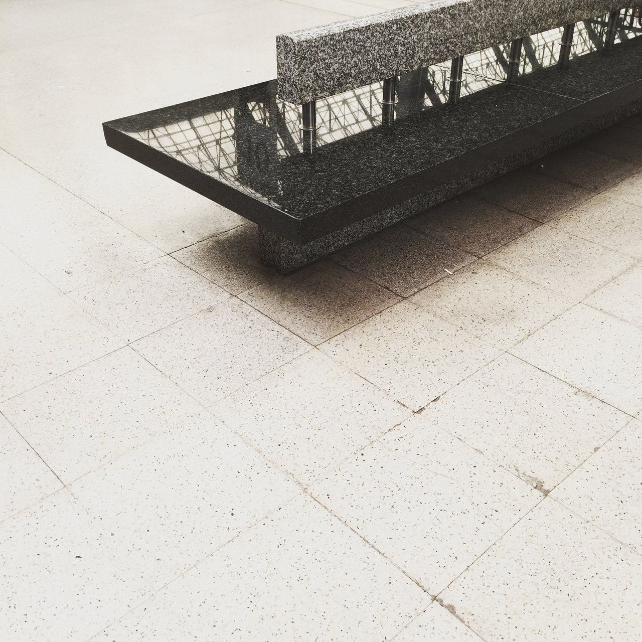 Concrete bench casting a hard shadow across a pale tiled concourse