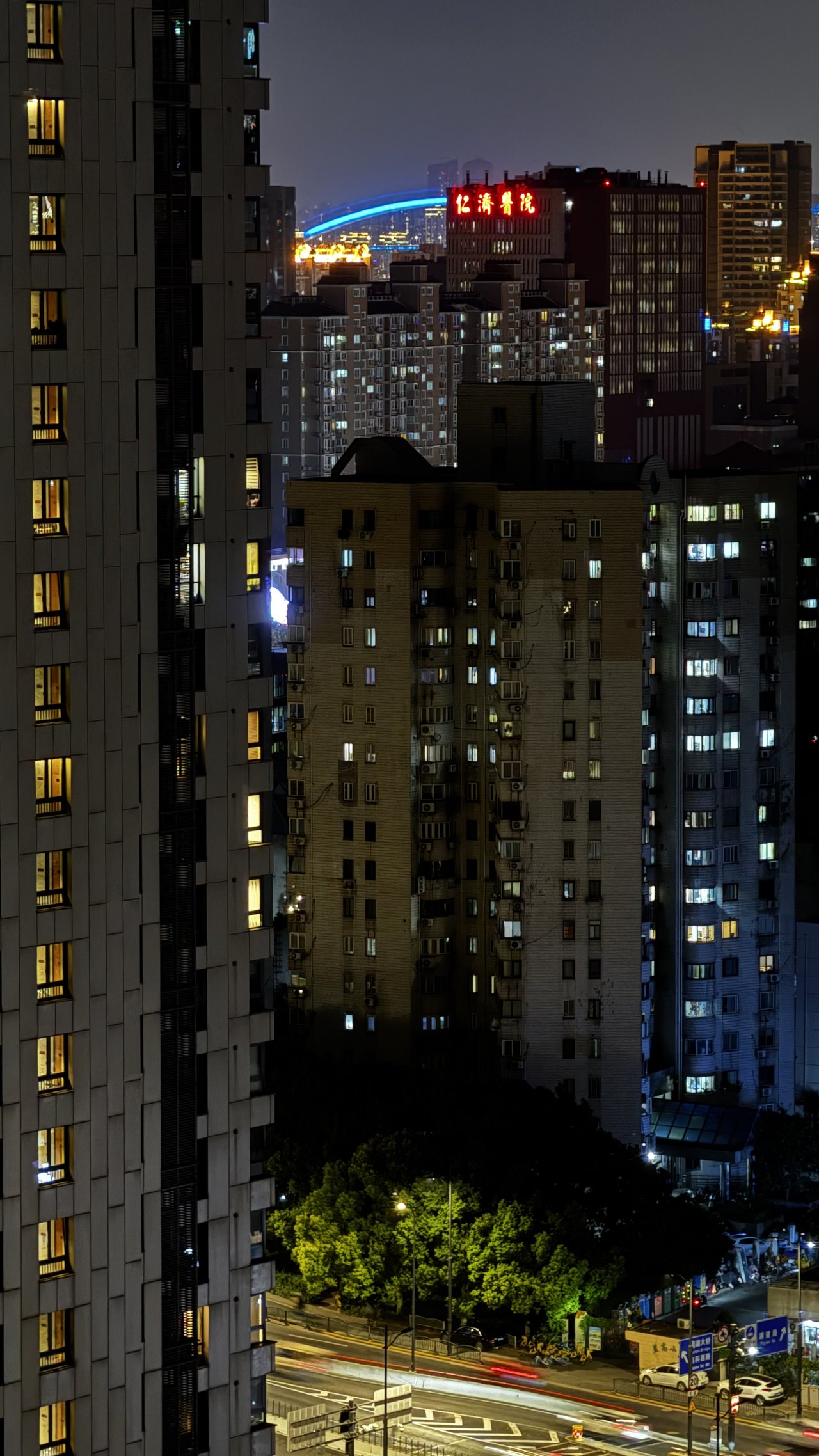 Apartment blocks at night, a hospital's red neon and a blue bridge arc beyond