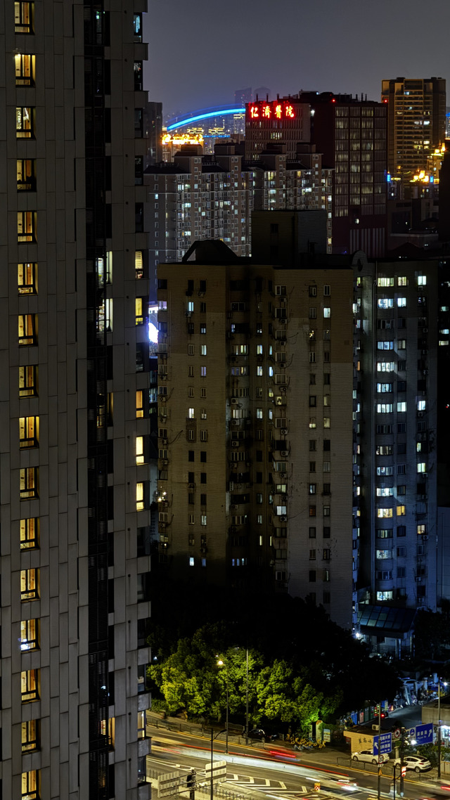 Apartment blocks at night, a hospital's red neon and a blue bridge arc beyond