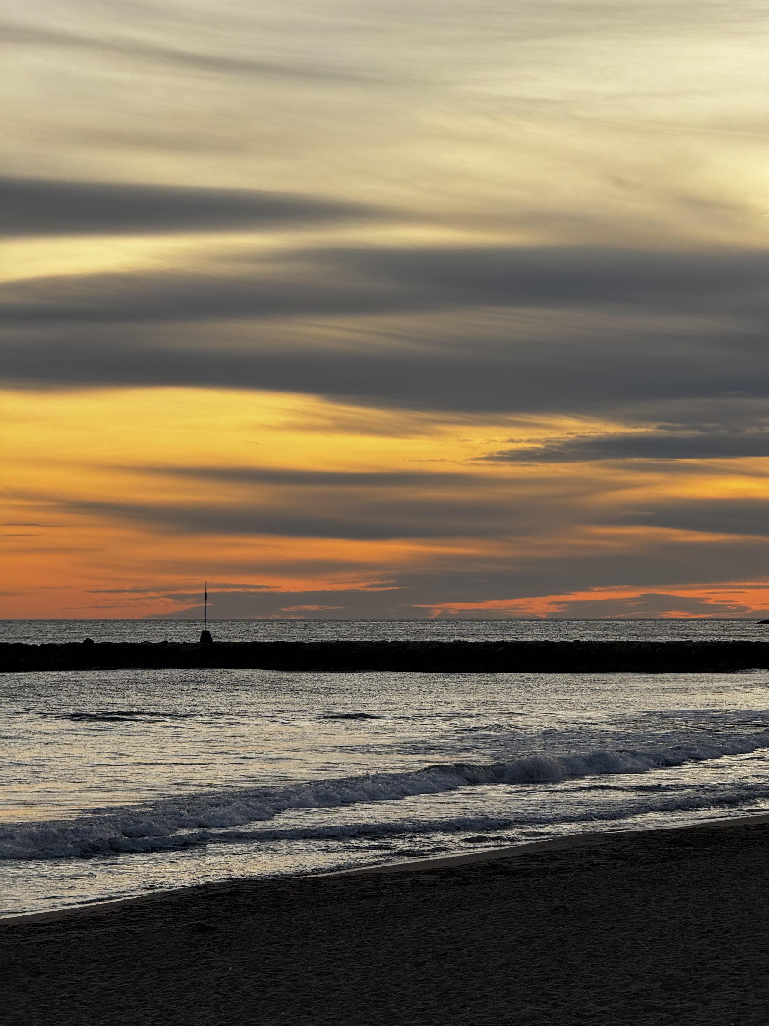 Banded sunset sky over a breakwater and its marker pole