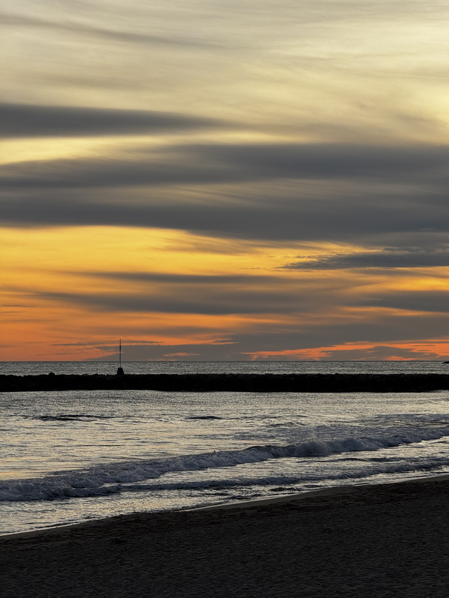 Banded sunset sky over a breakwater and its marker pole