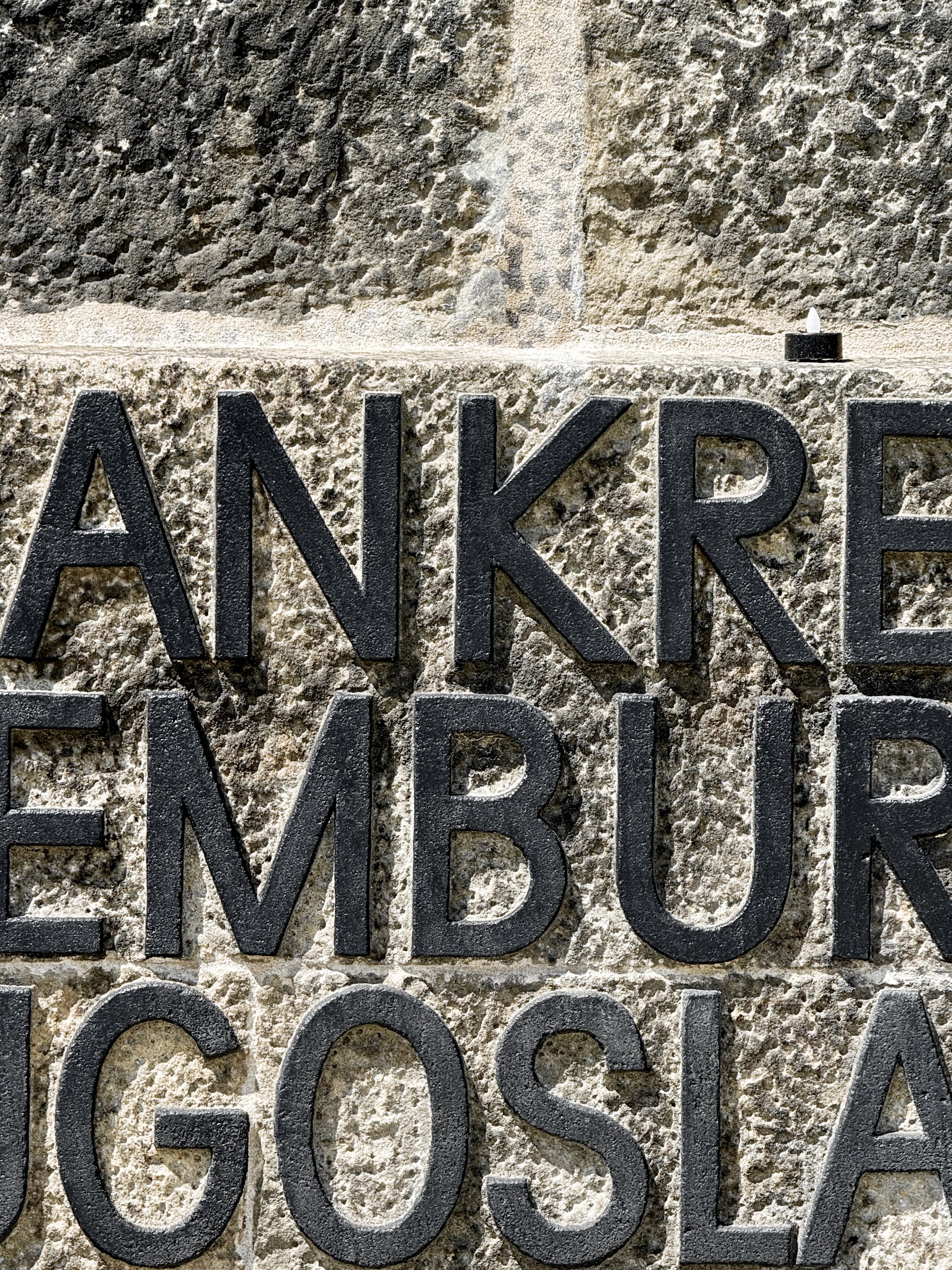 Cast-iron country names on the Dachau memorial wall, a small candle above