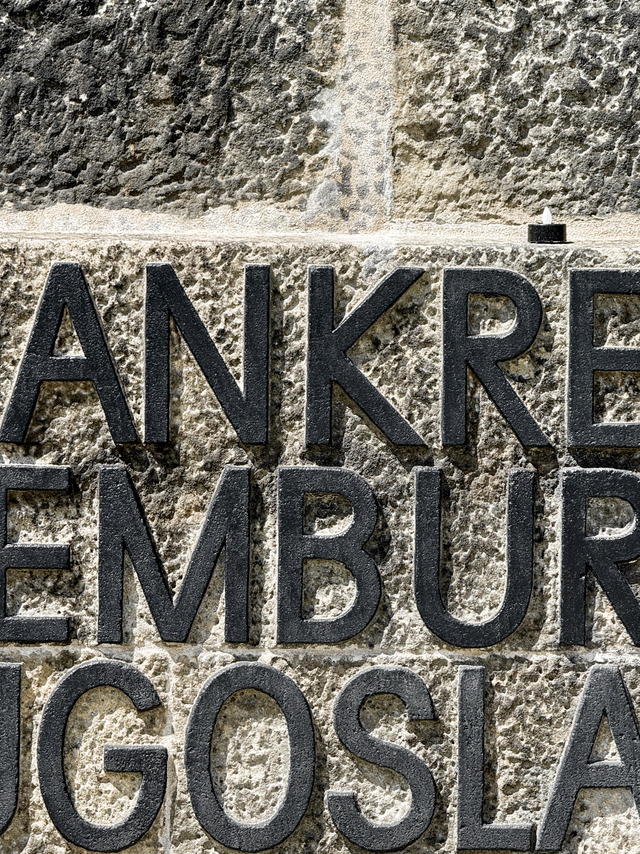 Cast-iron country names on the Dachau memorial wall, a small candle above