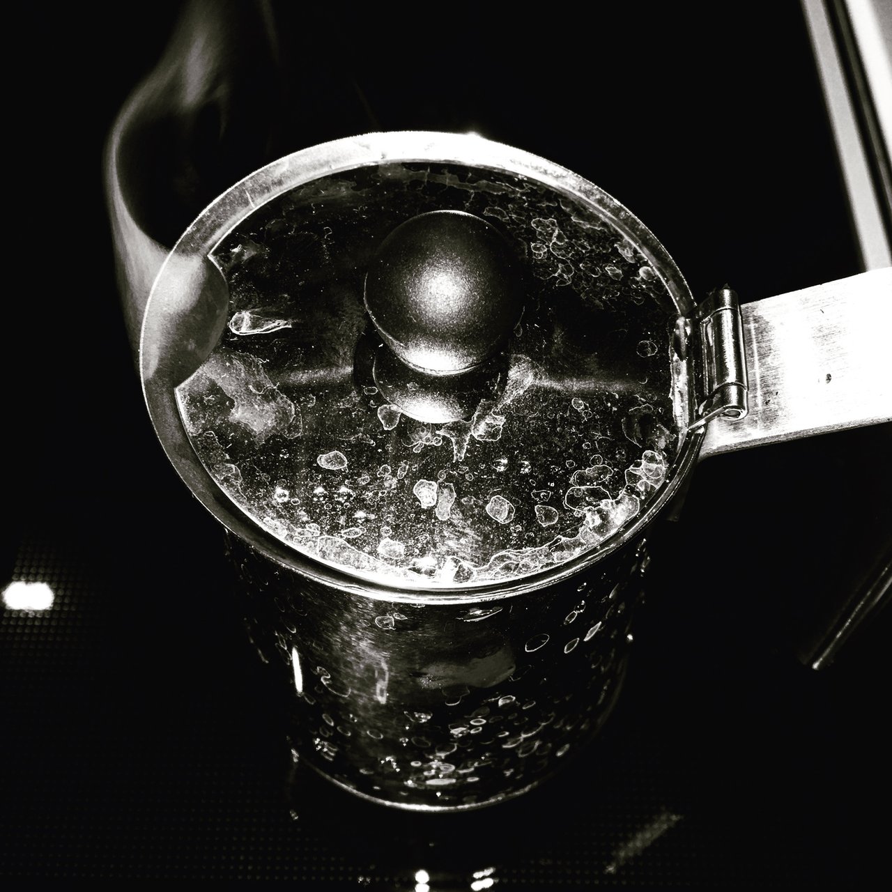Close-up of a metal coffee maker filled with water, lit hard against darkness