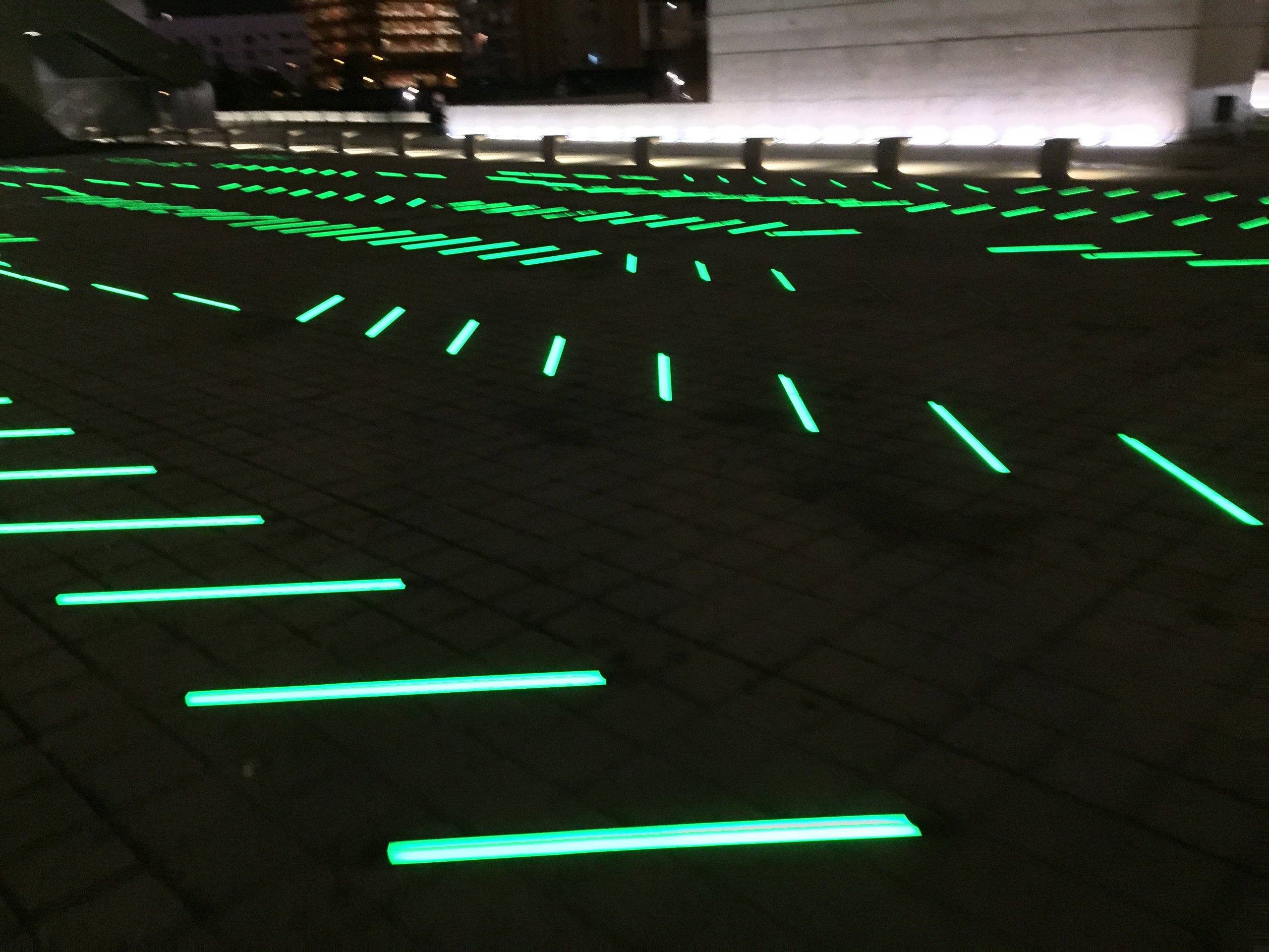 Green LED strips set into a dark pavement at night, receding in perspective