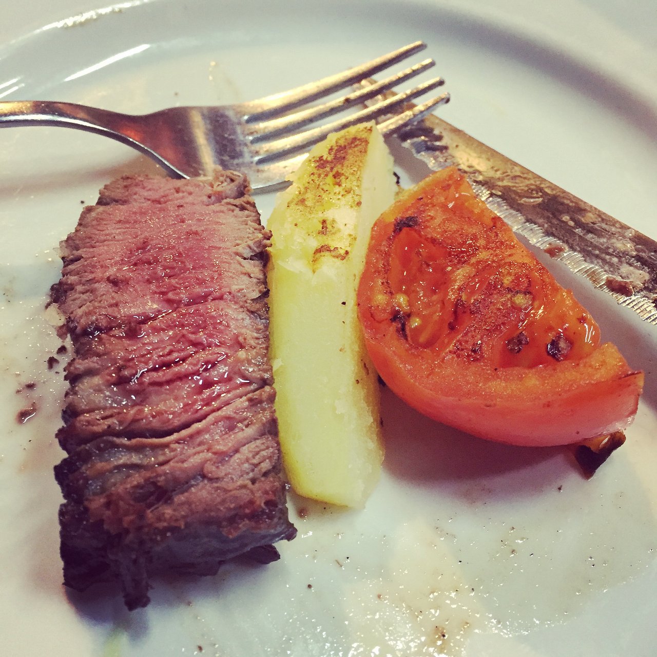 Sliced steak with potato and grilled tomato on a plate