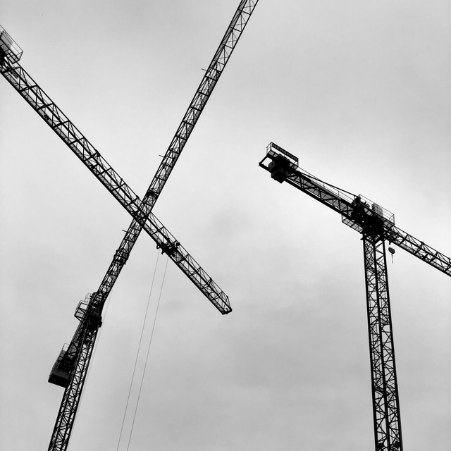 Four tower-crane jibs cross a flat grey sky, latticework interleaved