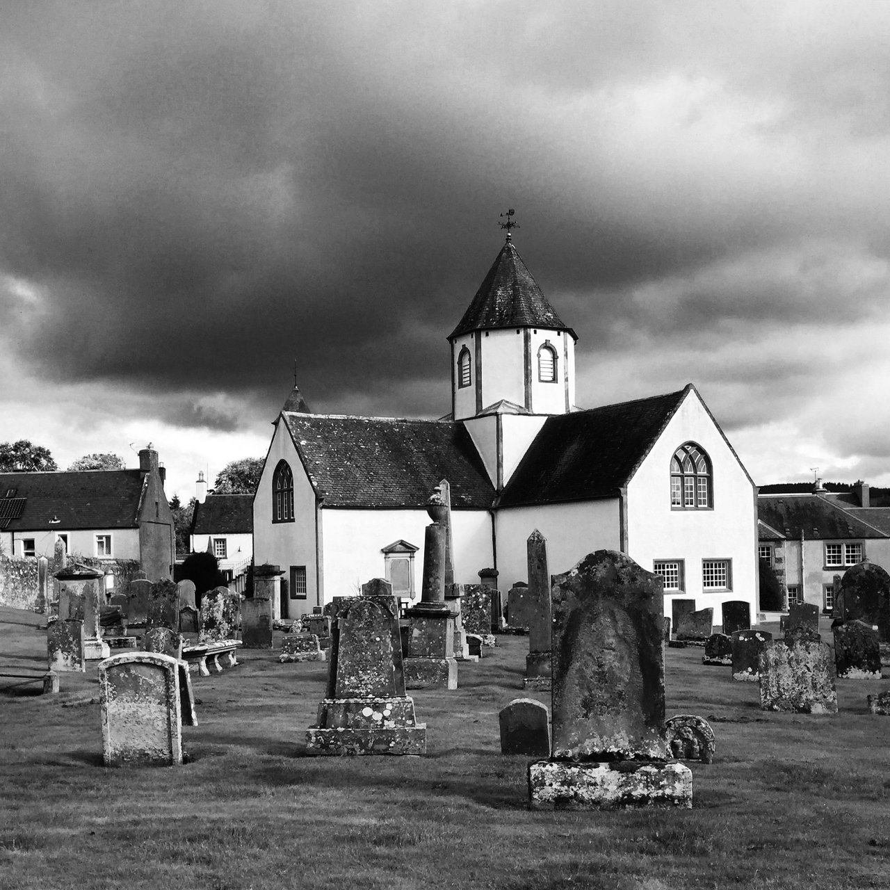 Whitewashed kirk behind leaning gravestones under heavy cloud
