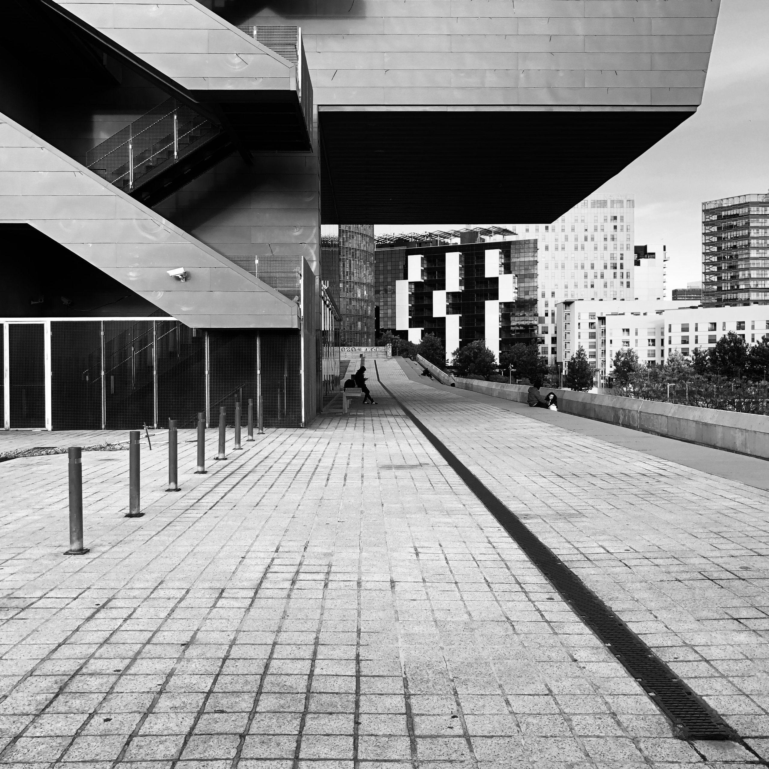 Cantilevered museum decks over a paved esplanade, figures beneath