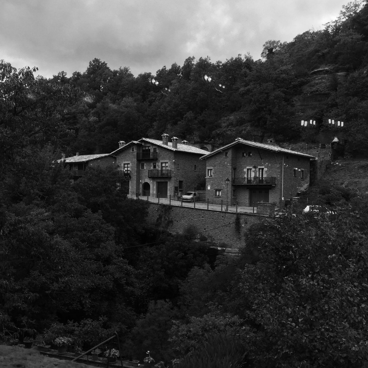 Stone houses stepped into a wooded hillside above Rupit, monochrome