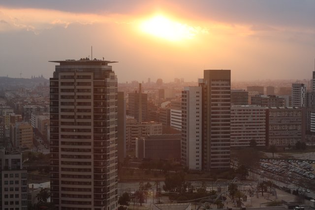 High-rise blocks under a hazy amber sunset, the sun low over the city