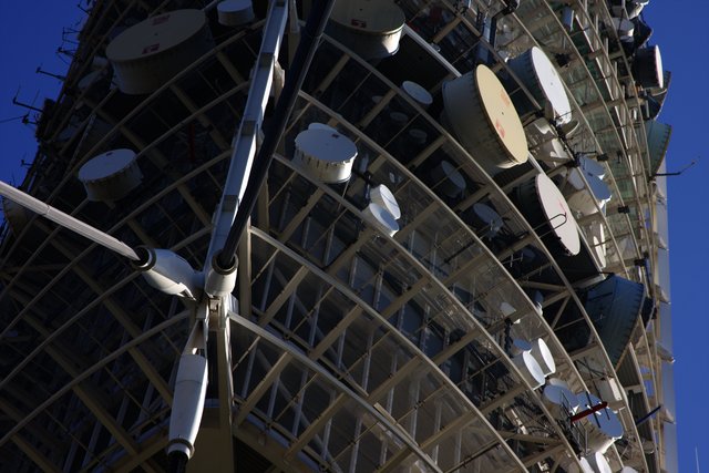 Underside of a telecommunications tower crowded with satellite dishes against deep blue sky