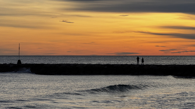 Two figures on the breakwater under an orange evening sky