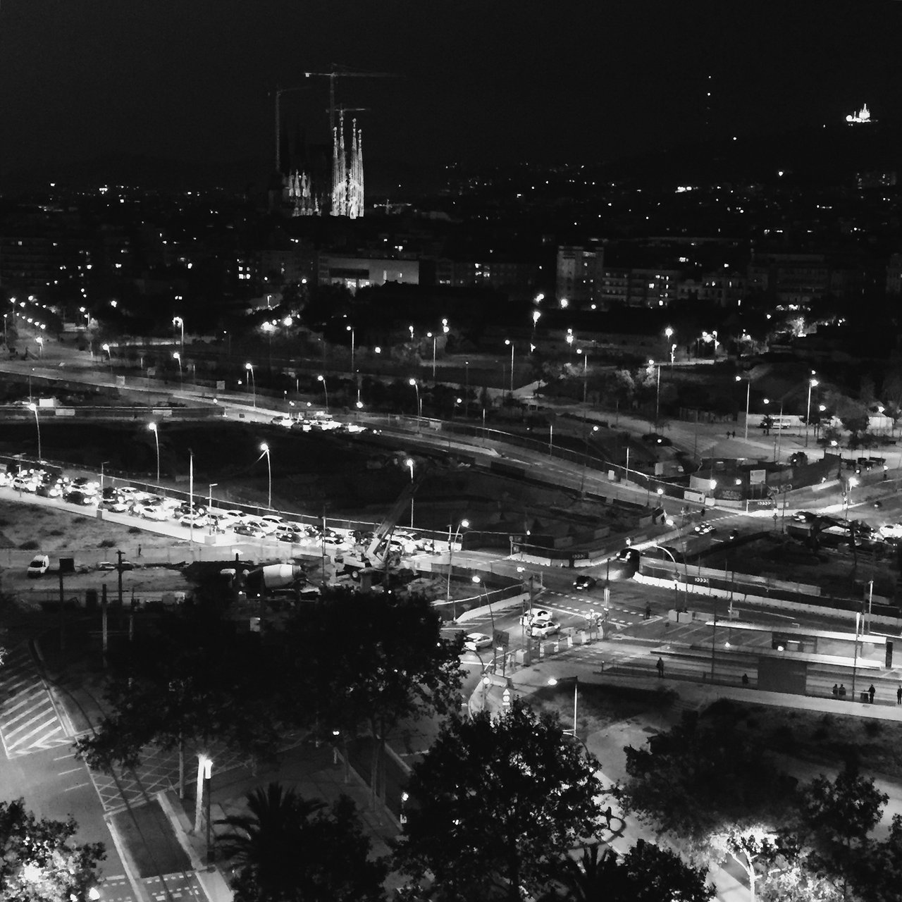 Barcelona at night from above, avenues glowing, spires on the skyline