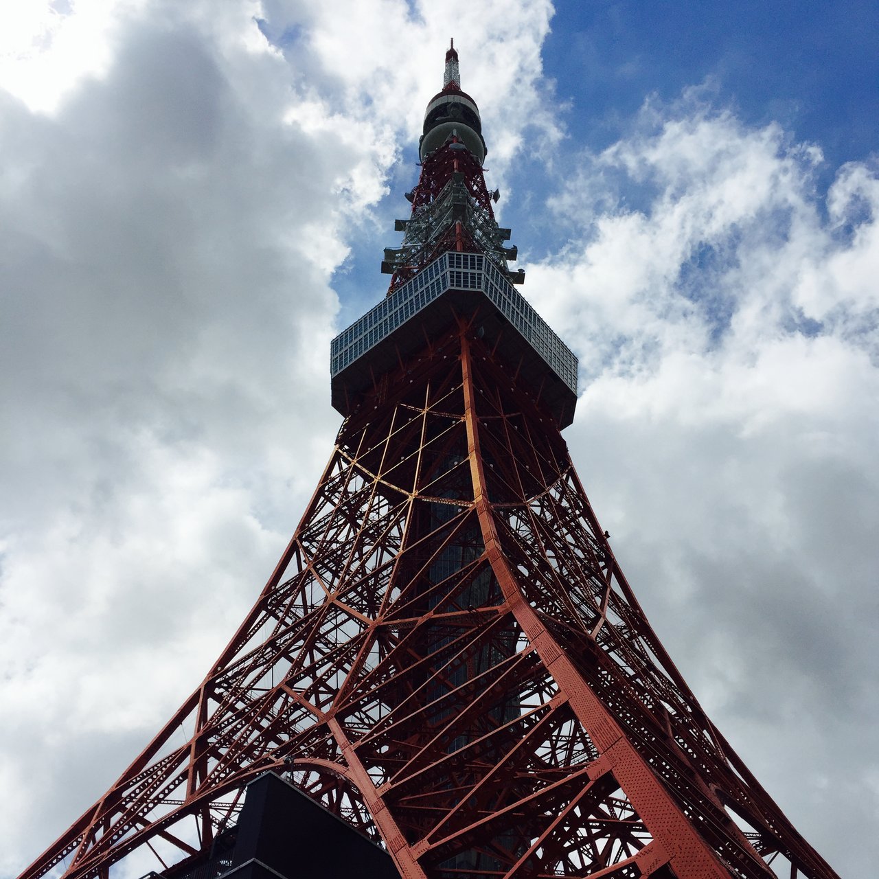 Red lattice tower rising into broken cloud, seen from directly below