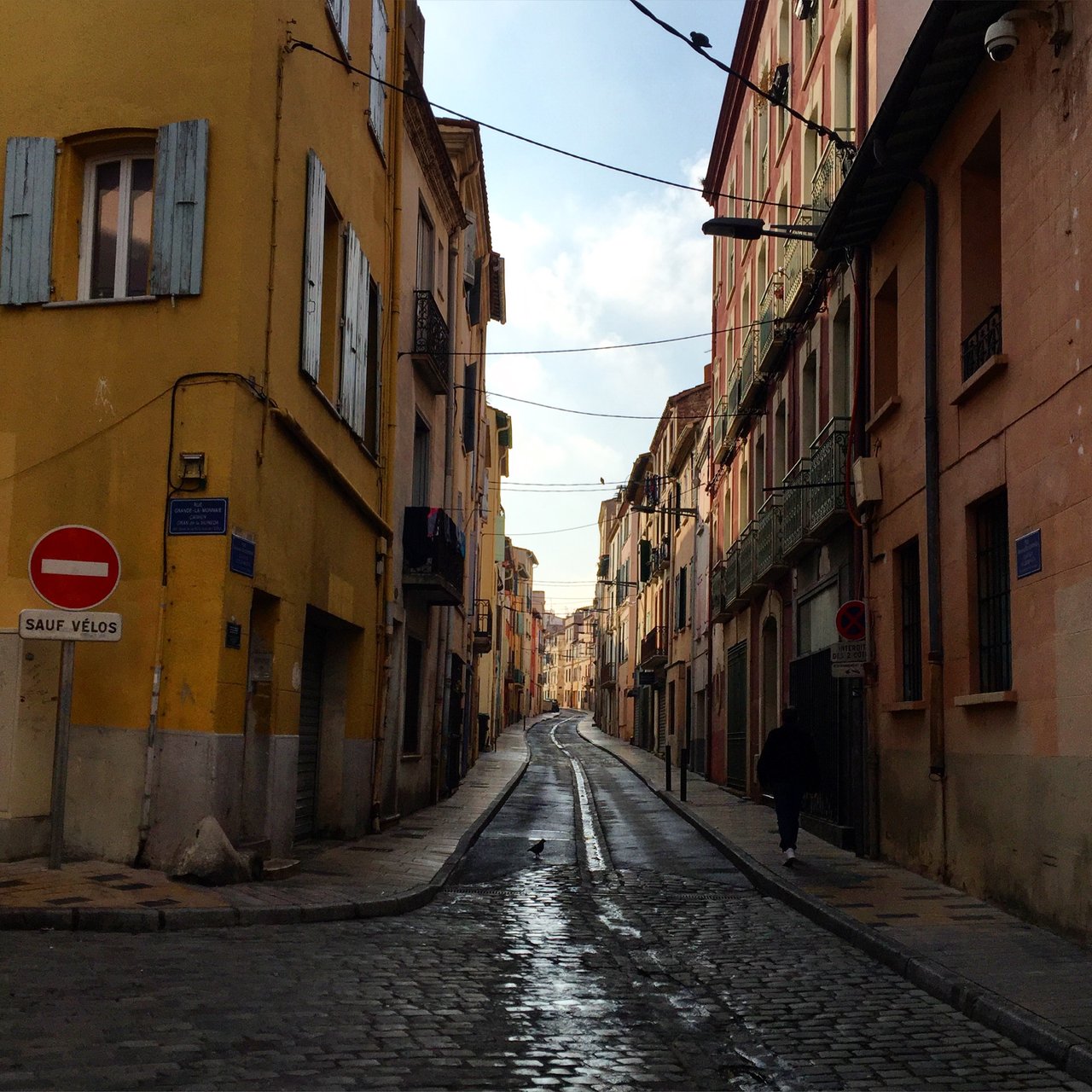 Wet cobbled street in a French town, no-entry sign, ochre and red shuttered façades