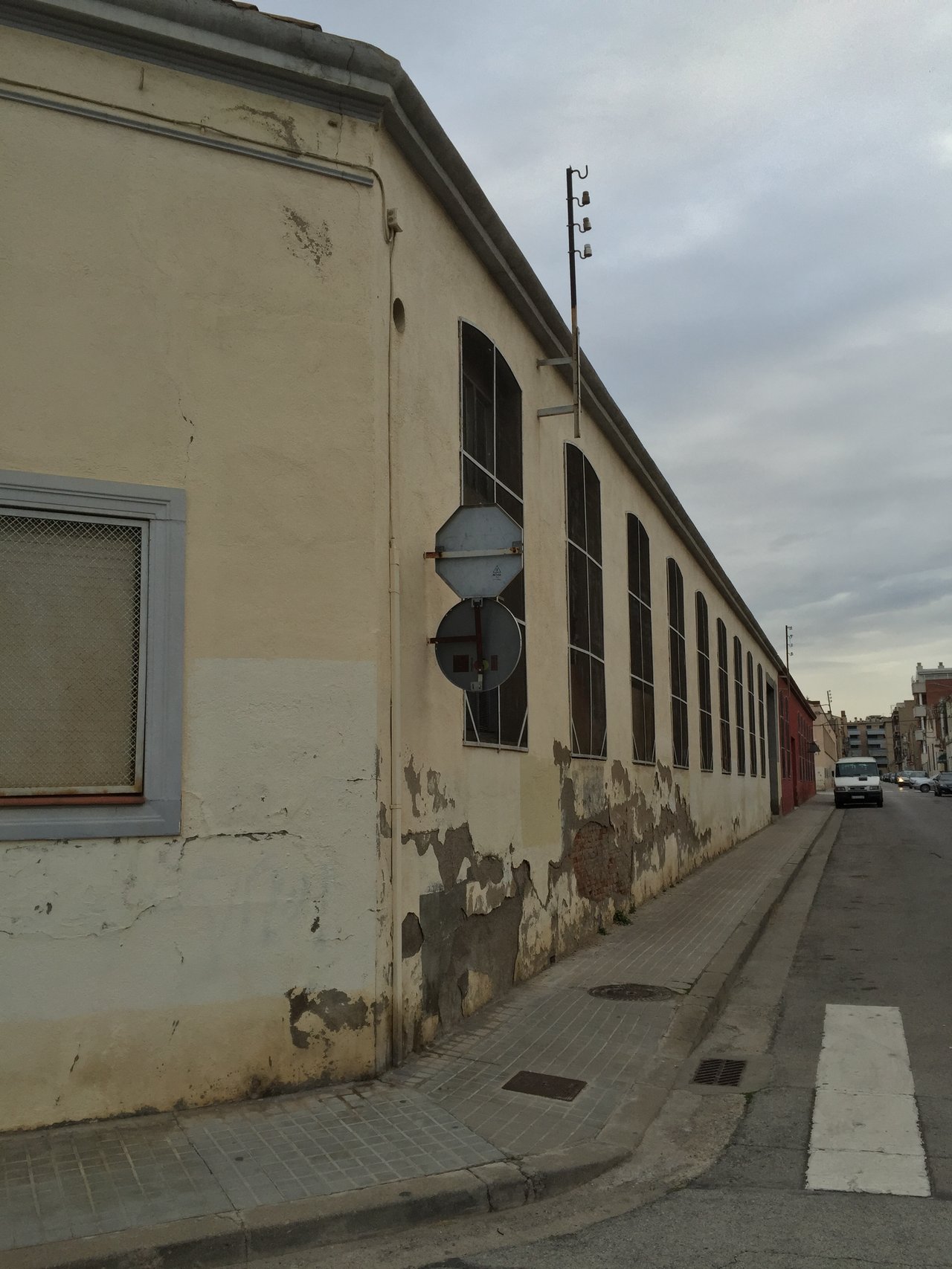 Long pale wall with peeling render along an empty street, overcast sky