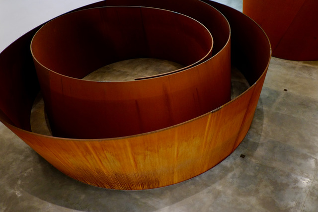 Weathered steel walls curl into a spiral on a concrete gallery floor
