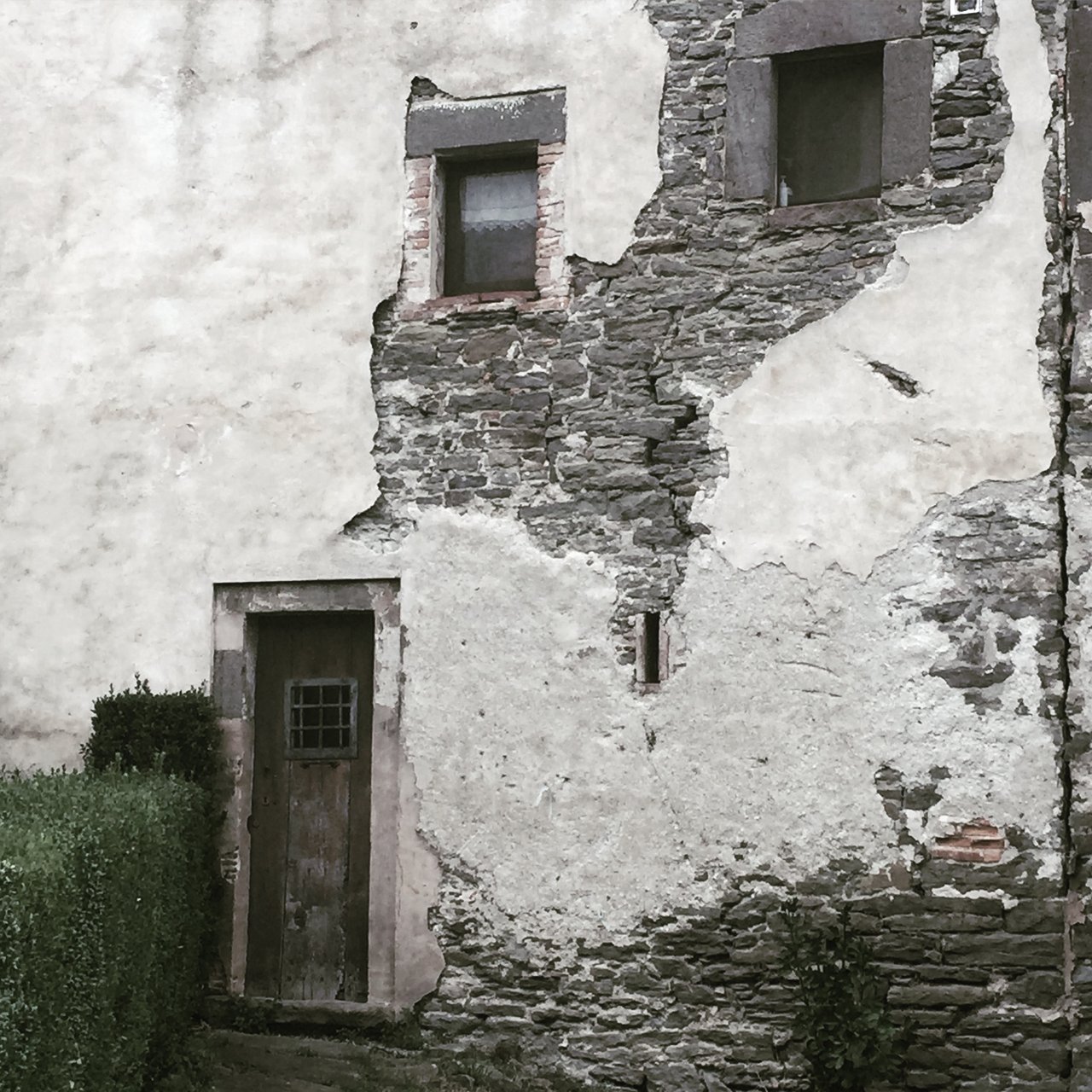 Stone wall where white render has fallen away around a small door
