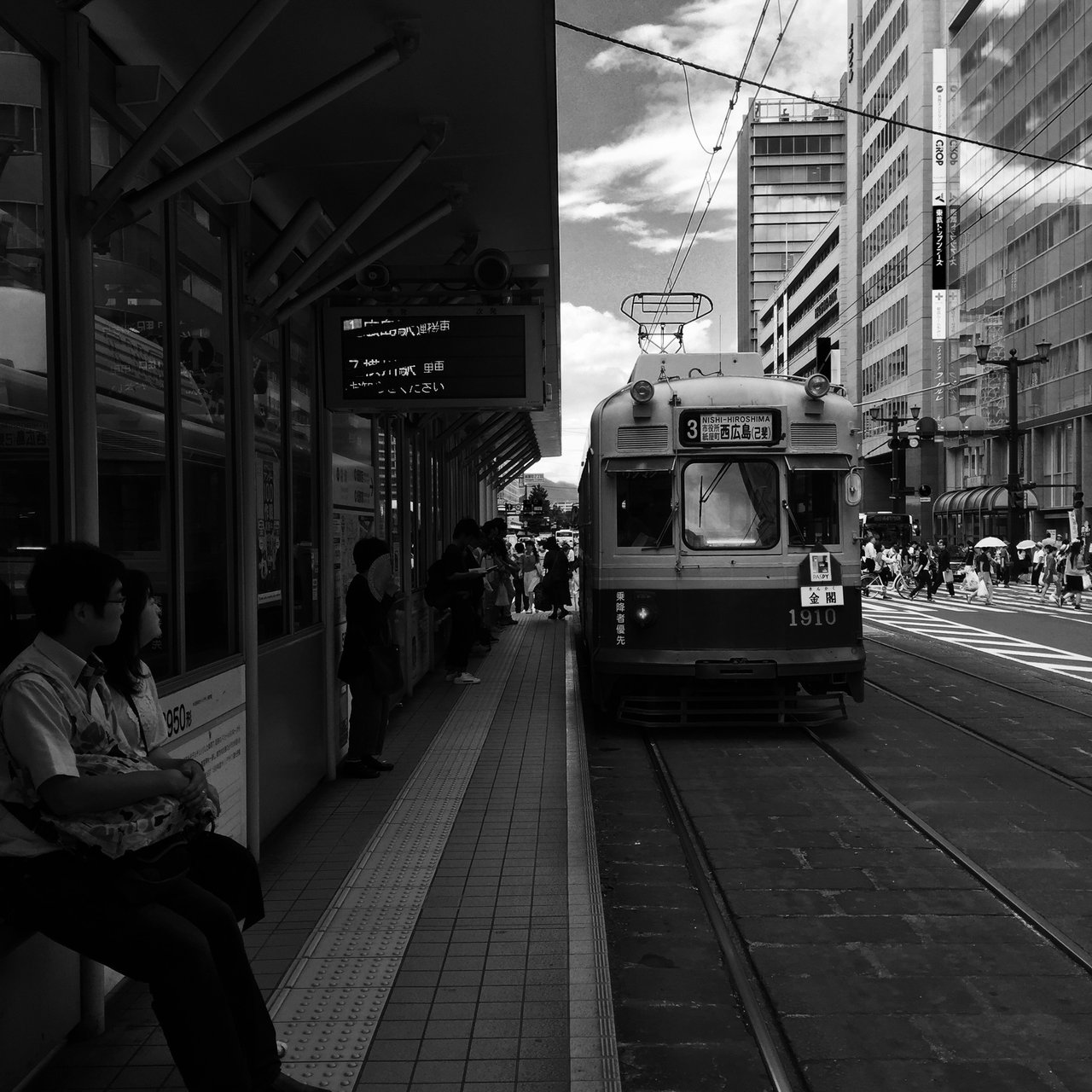 Tram waiting at a city stop in monochrome, passengers on the platform