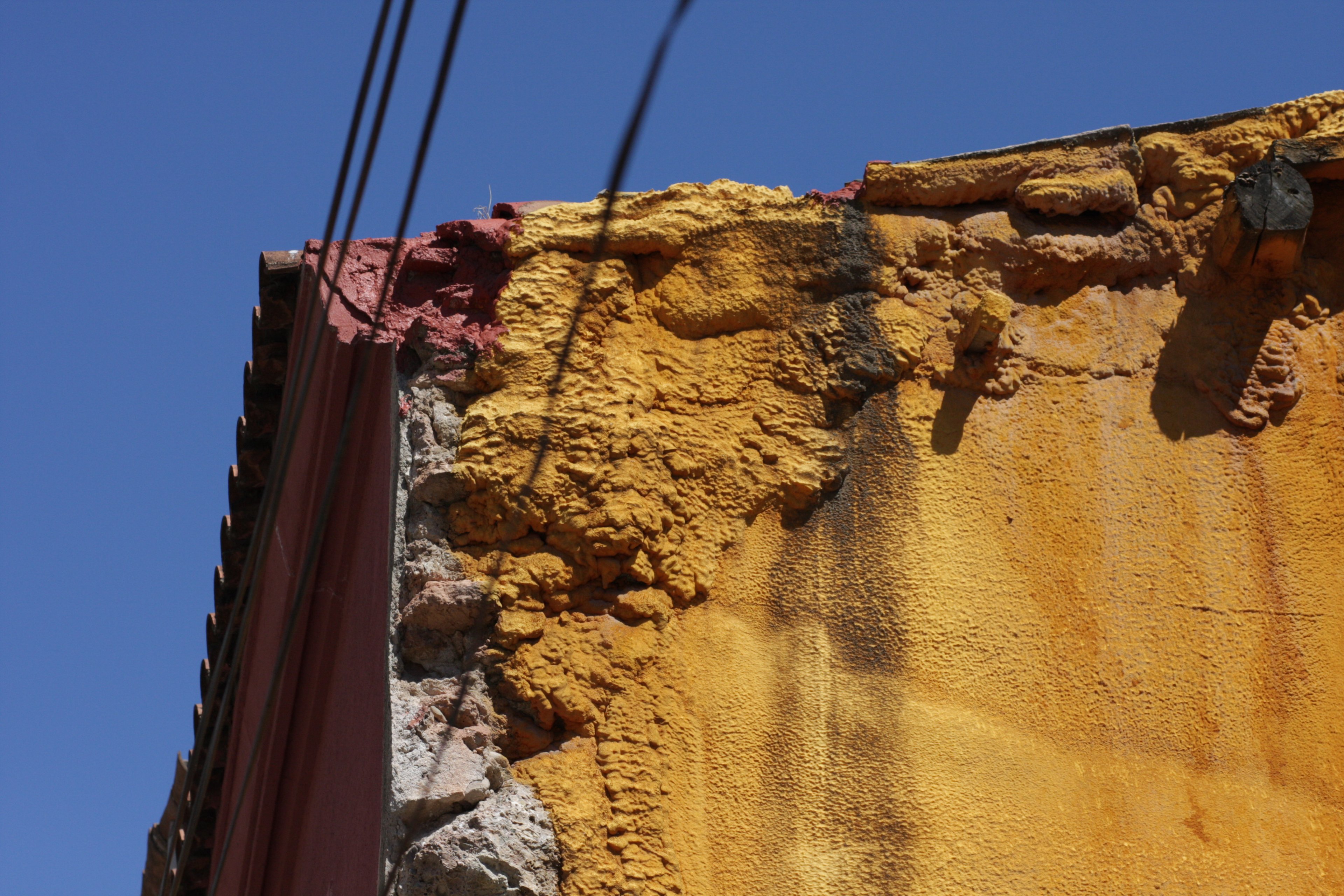 Crumbling ochre and pink wall corner under overhead wires against blue sky