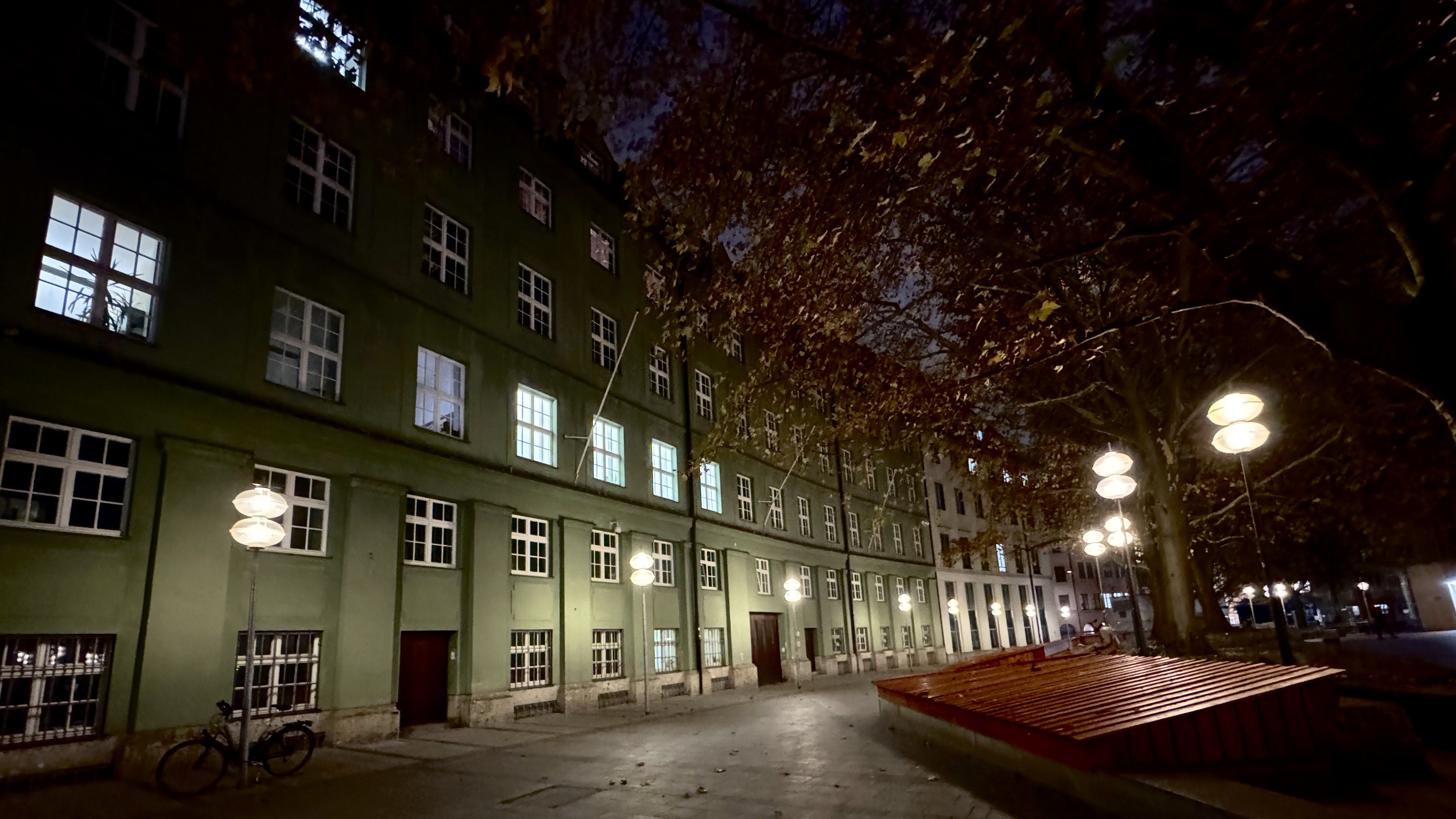 Glass-disc lamps light an empty square before a green municipal block