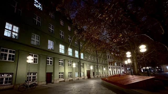 Glass-disc lamps light an empty square before a green municipal block