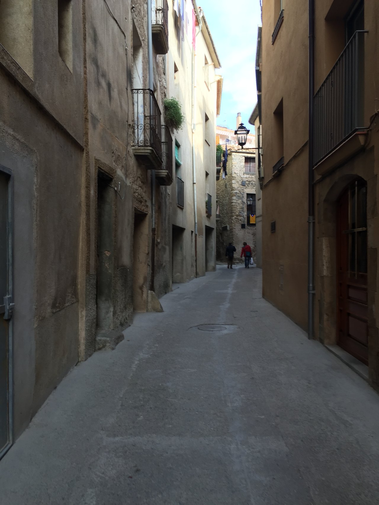 Narrow old-town street between stone and rendered buildings, two figures walking away