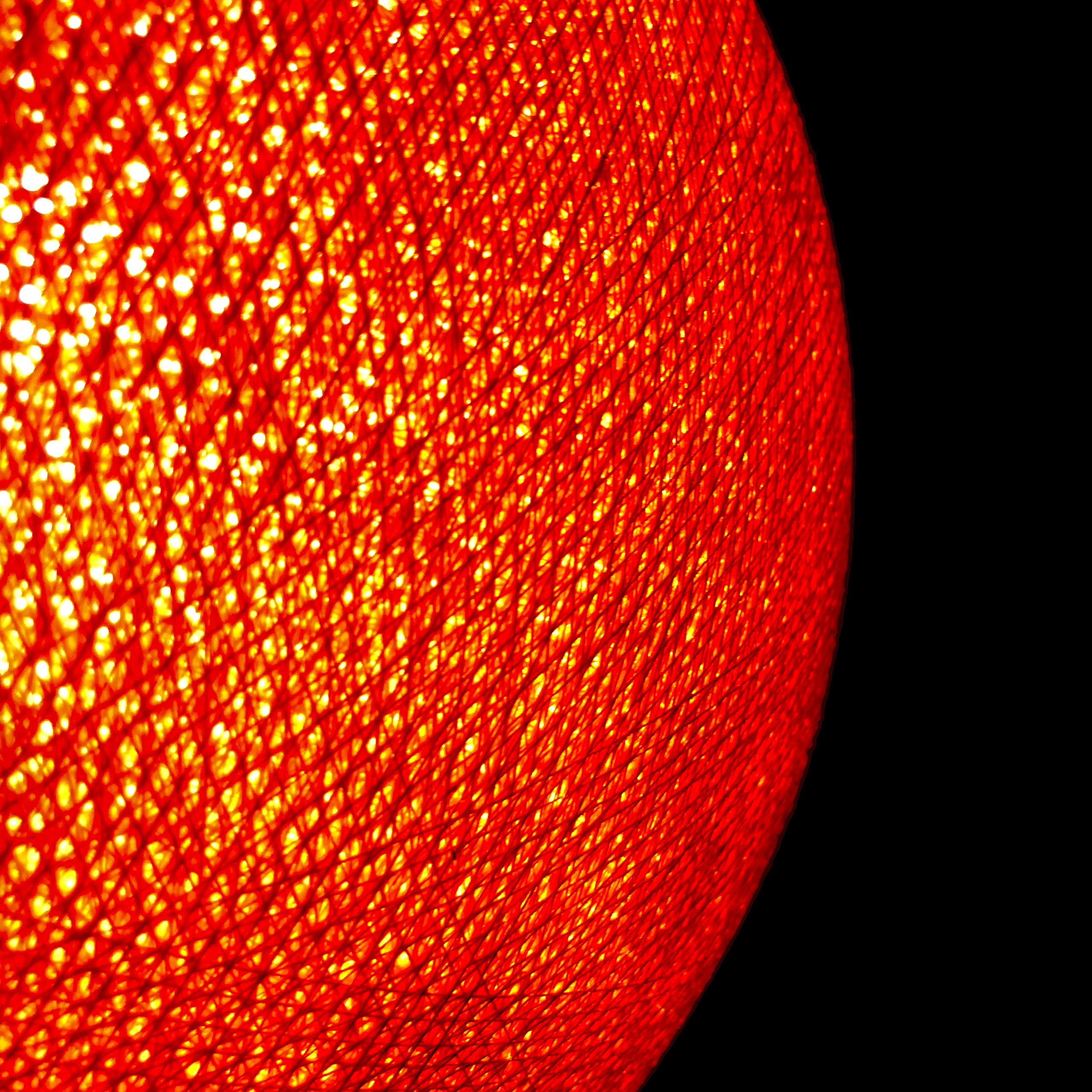 A woven lampshade burns orange, its crosshatched threads pricked with light