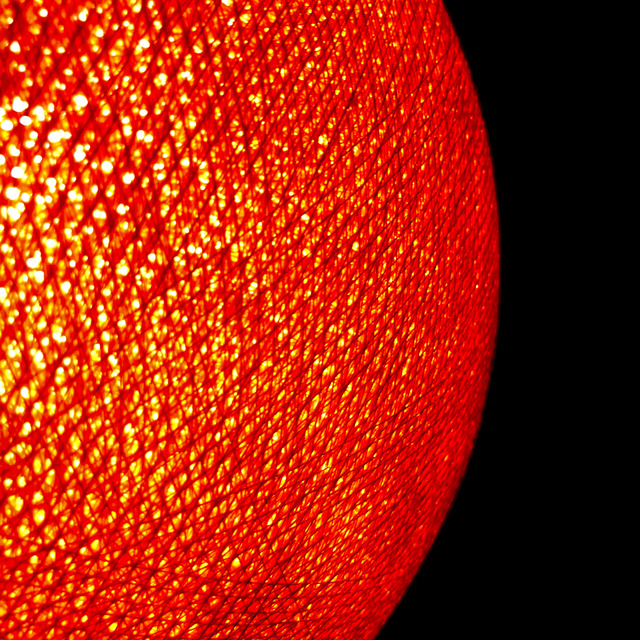 A woven lampshade burns orange, its crosshatched threads pricked with light