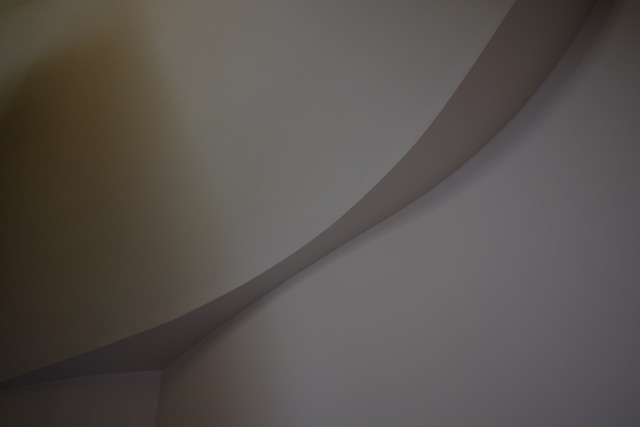 A pale plaster curve narrows to its waist where two walls meet in low light