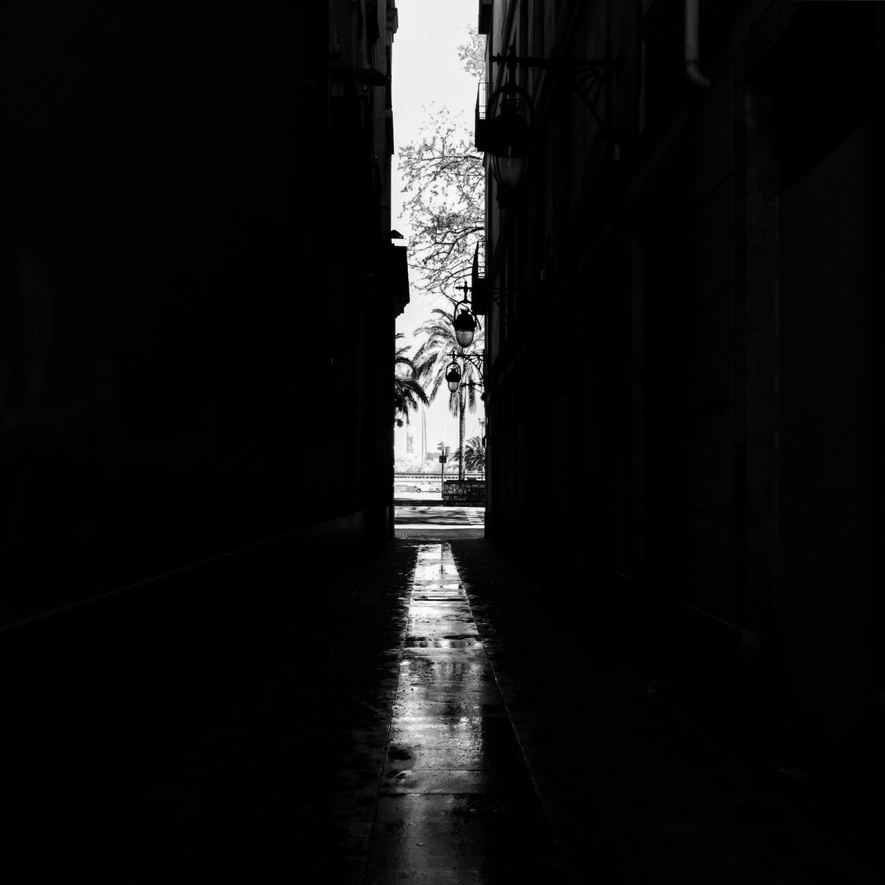 Dark alley in monochrome opening to a bright wet street beyond